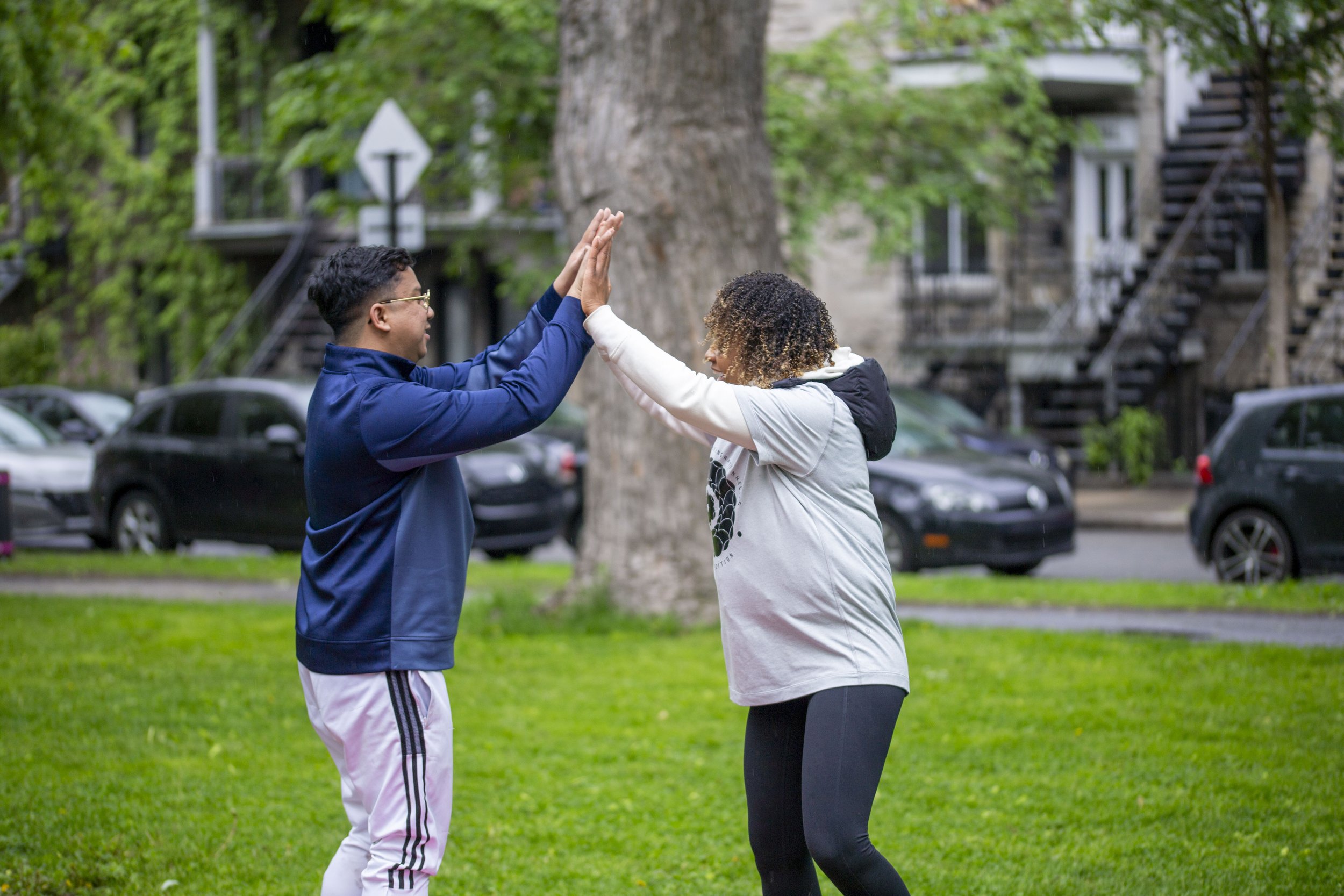 deux personnes faisant un geste de high five dans un parc avec des voitures garées en arrière-plan
