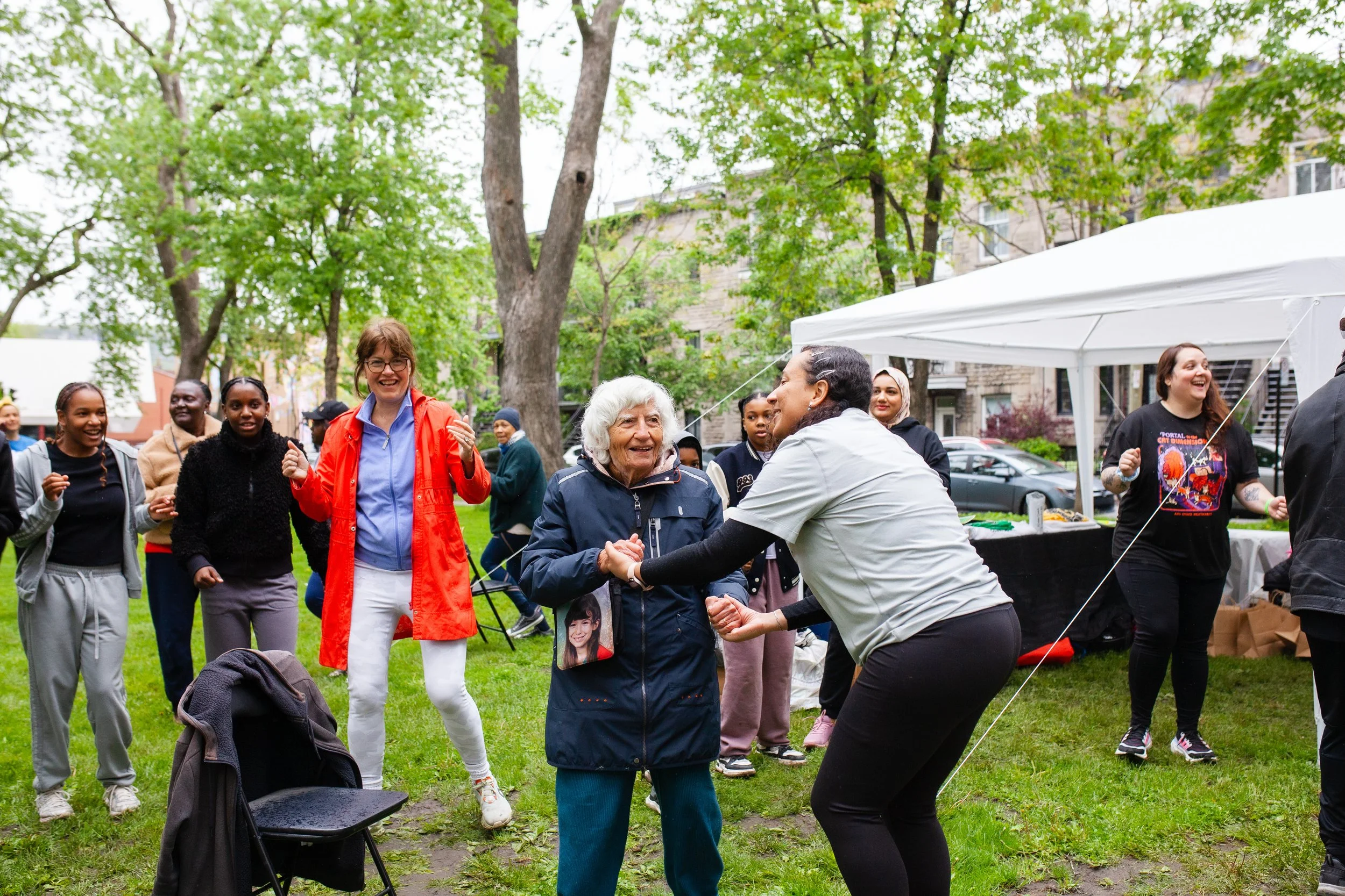 Groupe de personnes diverses joyeuses dans un parc, dansant et s'amusant lors d'une fête communautaire, avec une tente en arrière-plan.