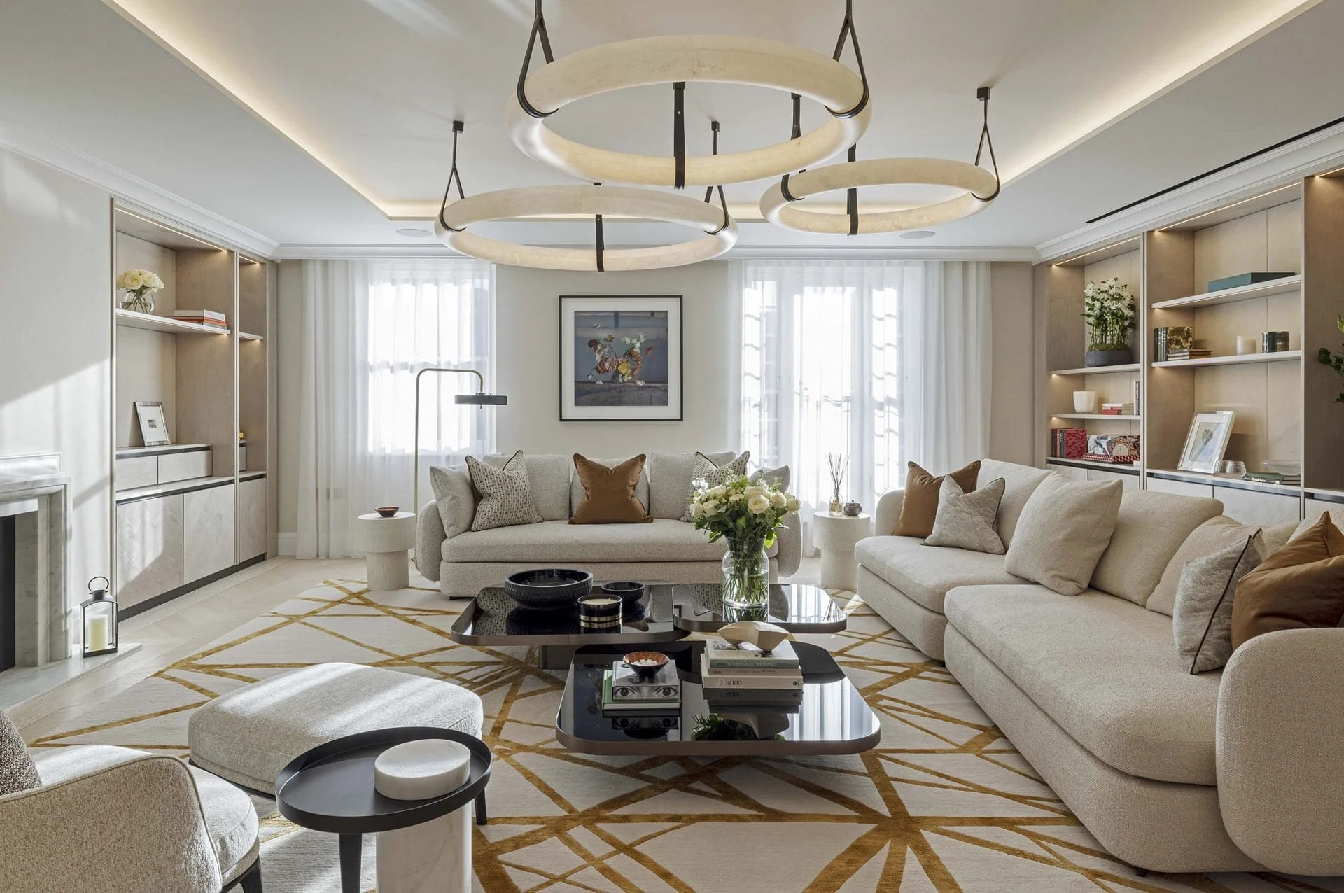 Bright and modern living room with beige sofas, patterned rug, coffee tables, built-in bookshelves, and circular ceiling light fixtures.