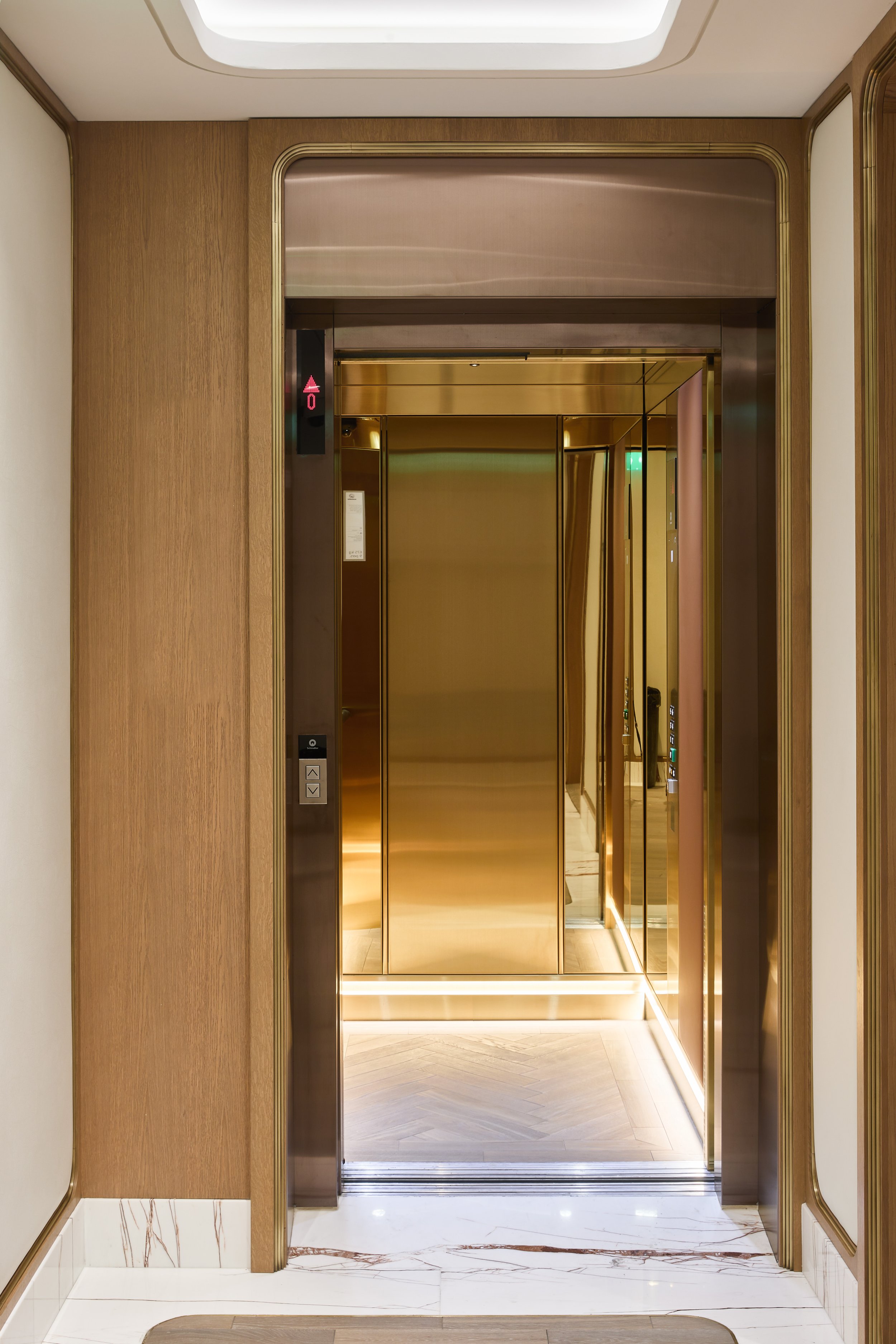An elevator with gold-colored doors and mirrored walls in a modern interior.