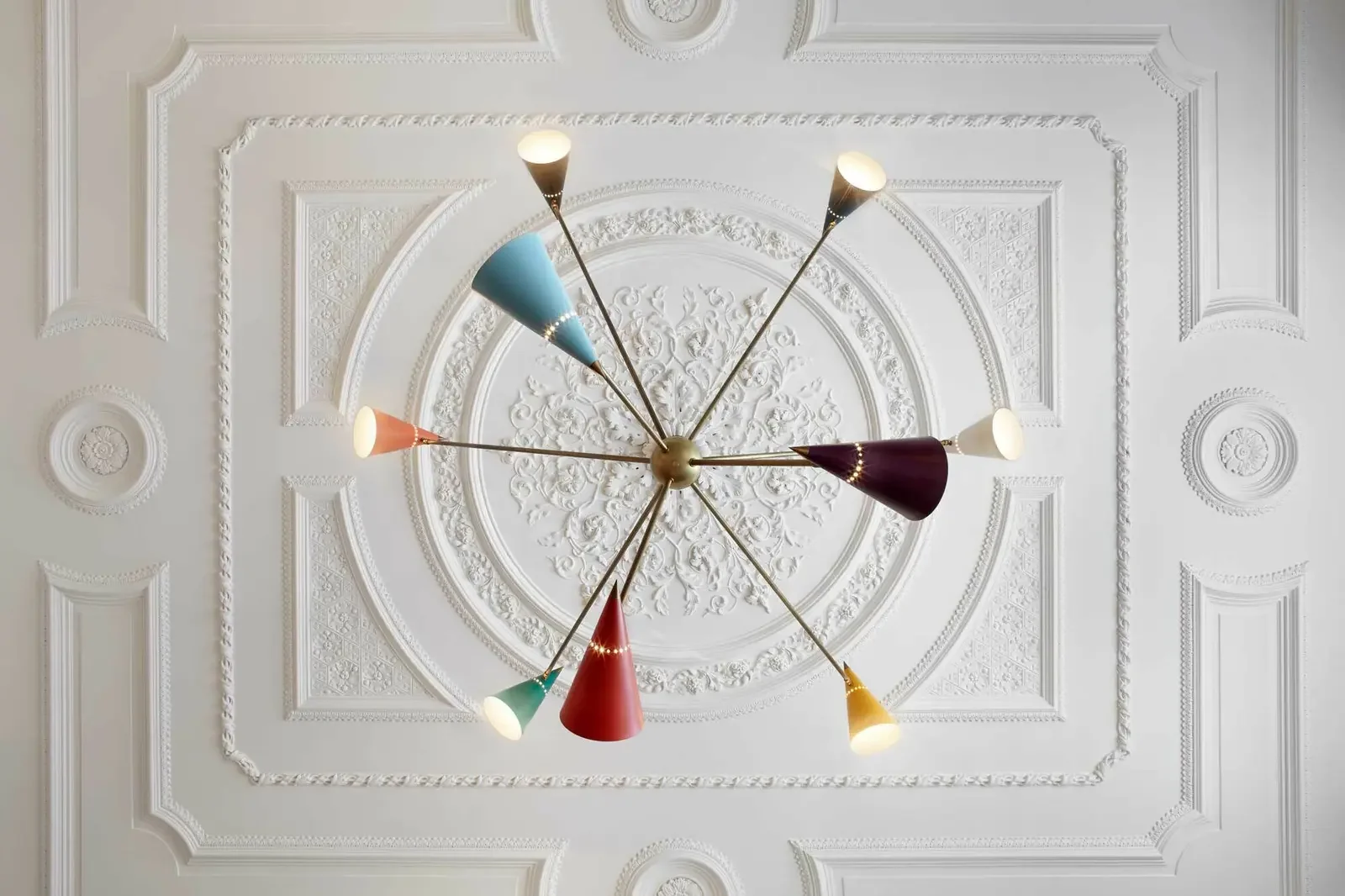 Colorful modern chandelier hanging from an ornate white ceiling with intricate molding.