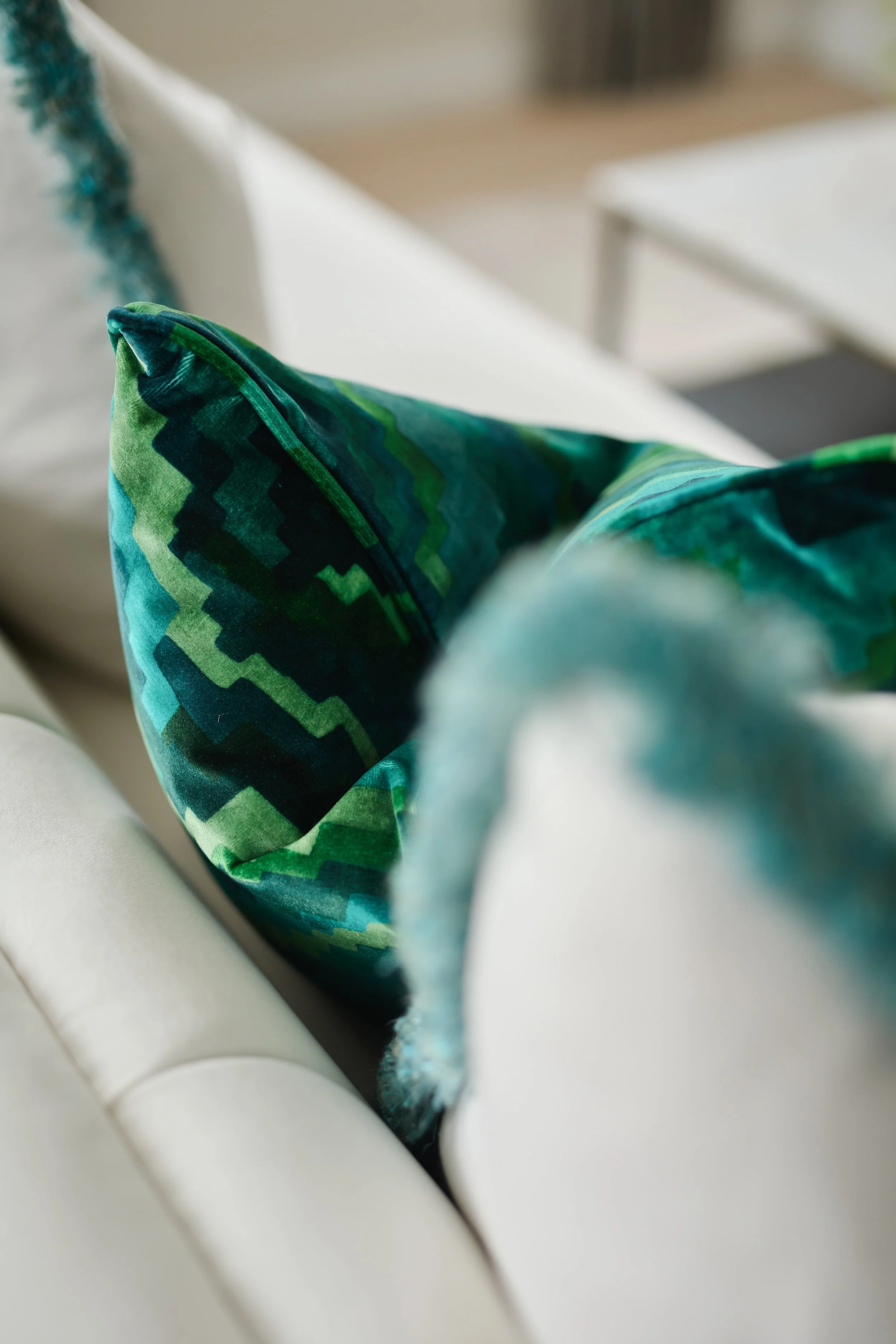A close-up of a green and blue patterned throw pillow on a white sofa.