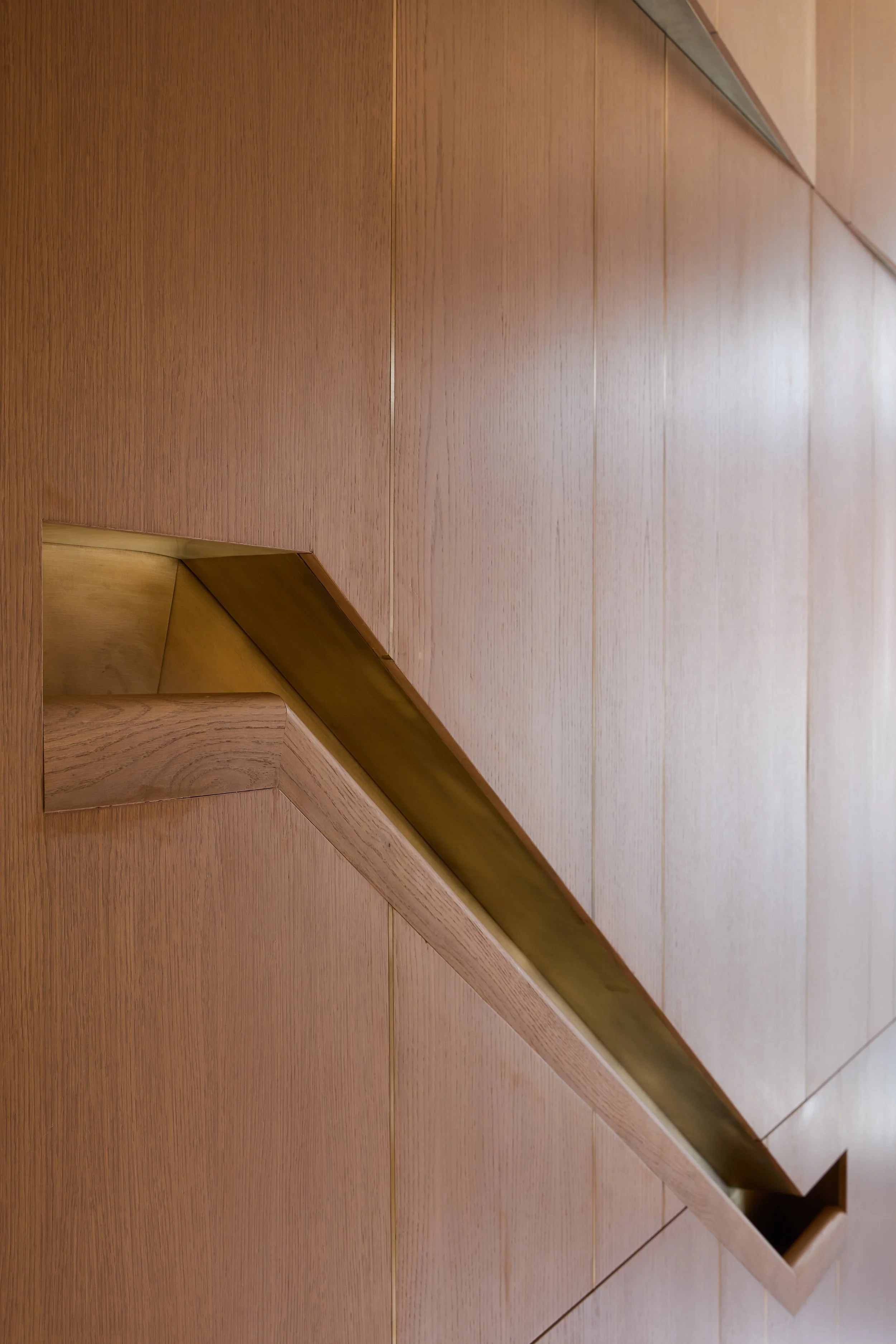 A close-up of a modern wooden staircase with a sleek handrail, viewed from above.