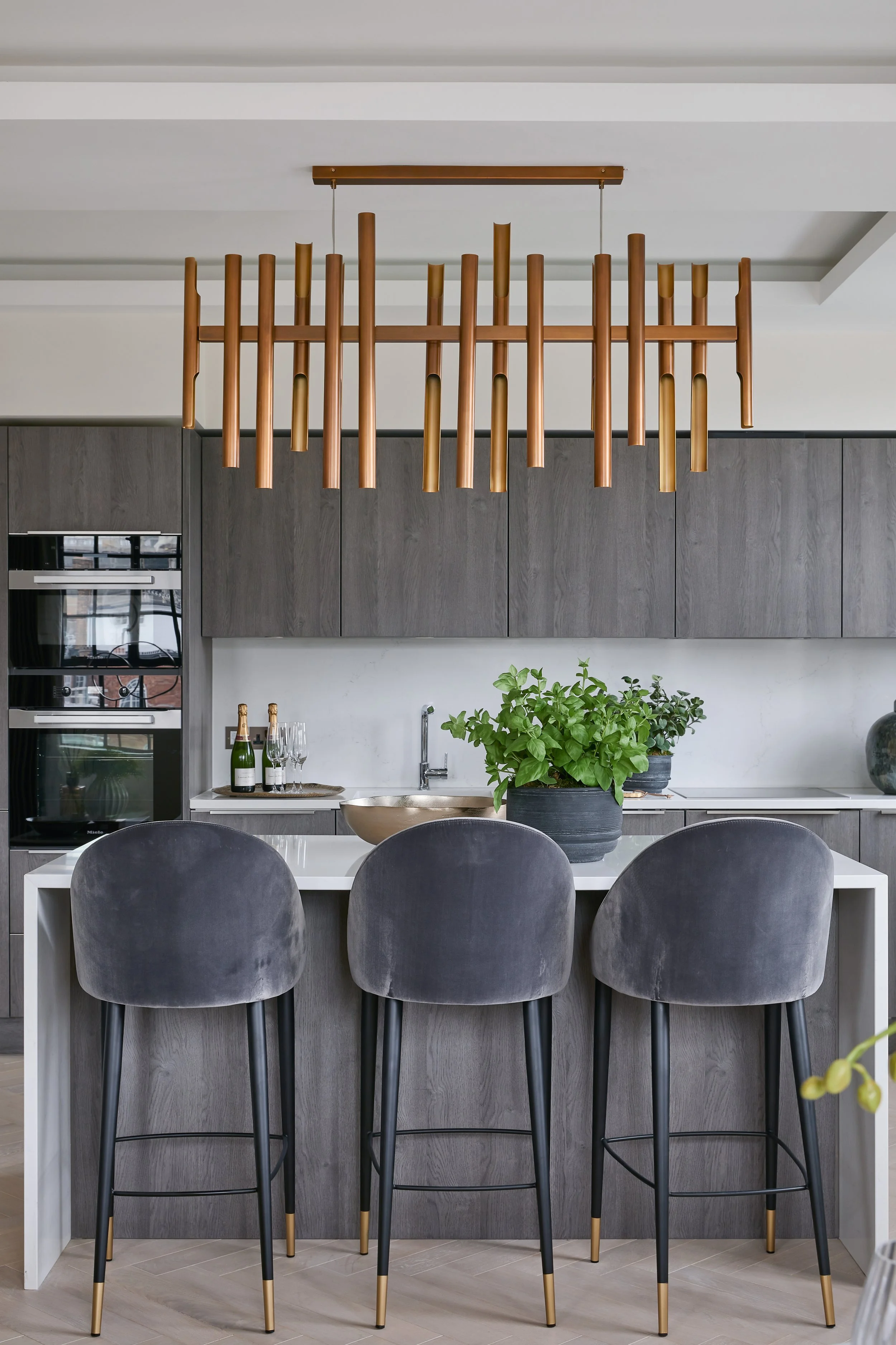 Modern kitchen with gray cabinets, black barstools, and a white kitchen island, decorated with green plants and two bottles of wine.