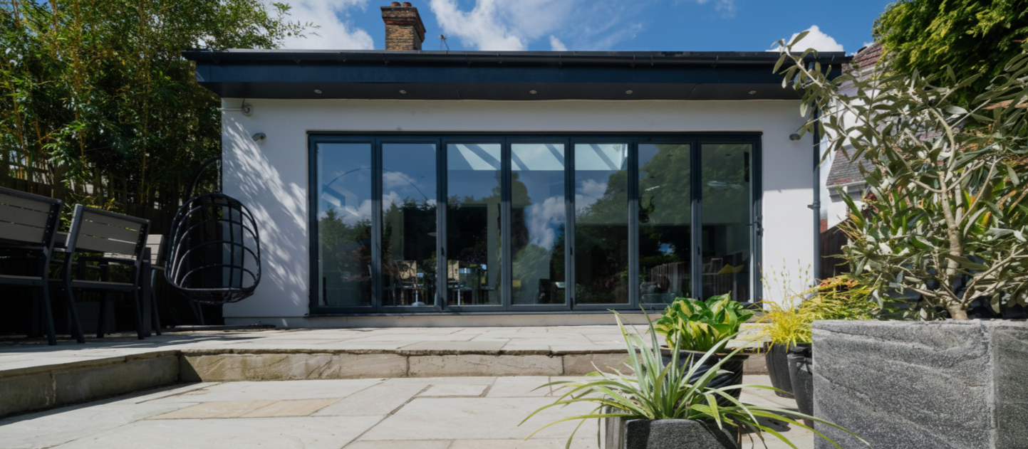 Modern house with large glass sliding doors, patio furniture, and potted plants in a backyard setting.