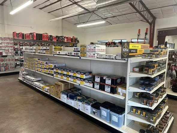 Hardware store aisle with shelves stocked with power tools, accessories, and storage bins, under industrial lighting in a spacious retail store.