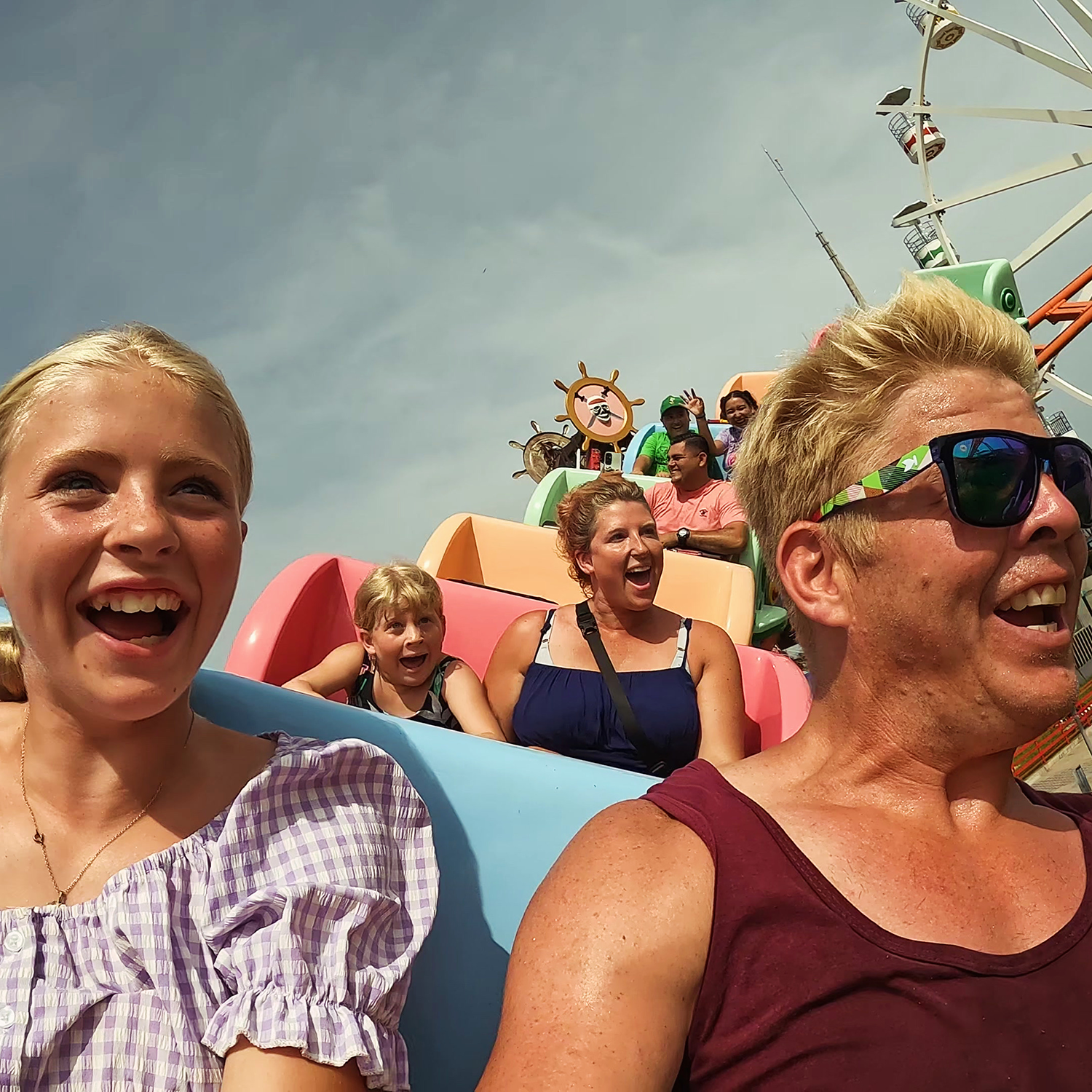 Gulyas family riding a colorful amusement park roller coaster, smiling and enjoying the ride on a sunny day.