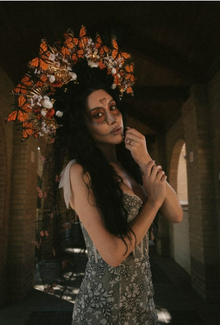 Women wearing a butterfly crown, with Sugar Skull makeup, and she is holding her hand. 
