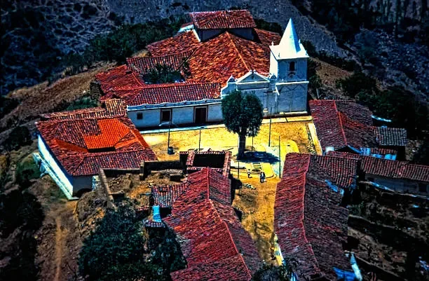 Aerial view of a hillside village with red-tiled roofs and a white church with a steeple at the center.