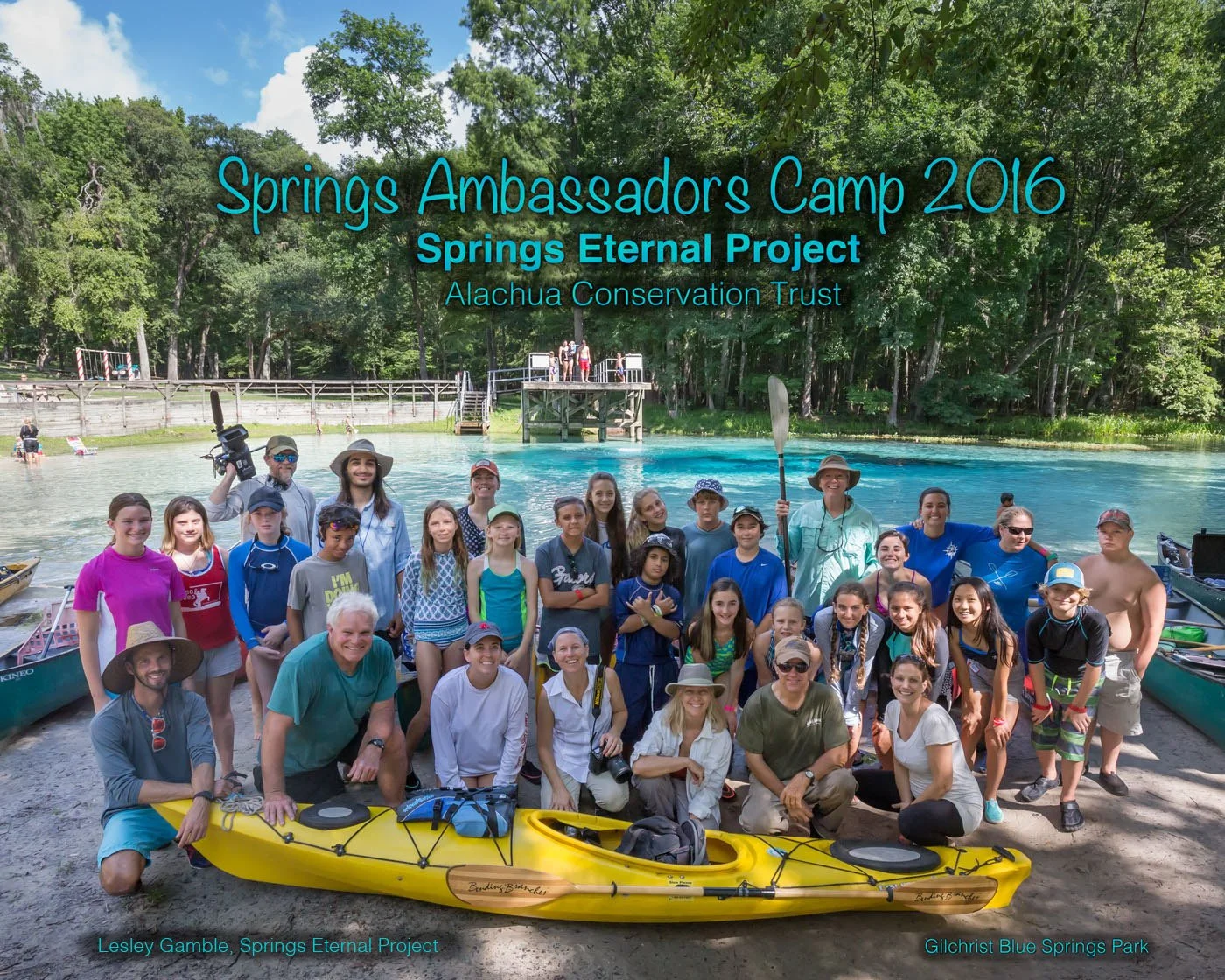 A group of children and adults pose by a bright blue freshwater spring with kayaks in the foreground and a wooden dock behind them. Overlaid text reads “Springs Ambassadors Camp 2016,” “Springs Eternal Project,” and “Alachua Conservation Trust.”