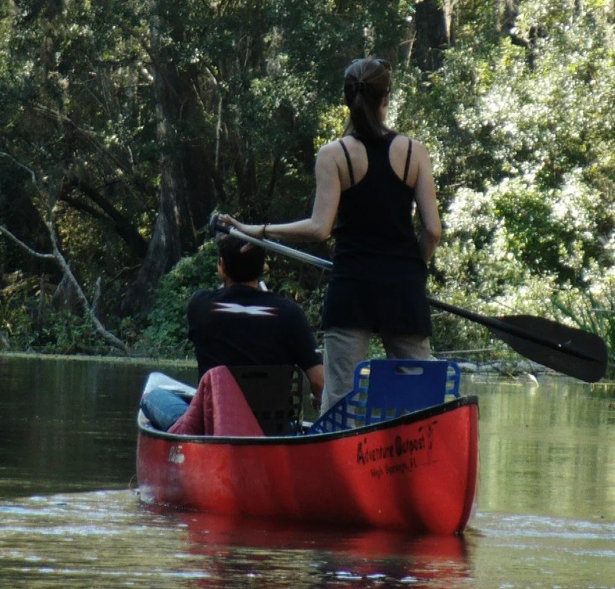 Two people paddling a red canoe along a shaded section of the Ichetucknee River.