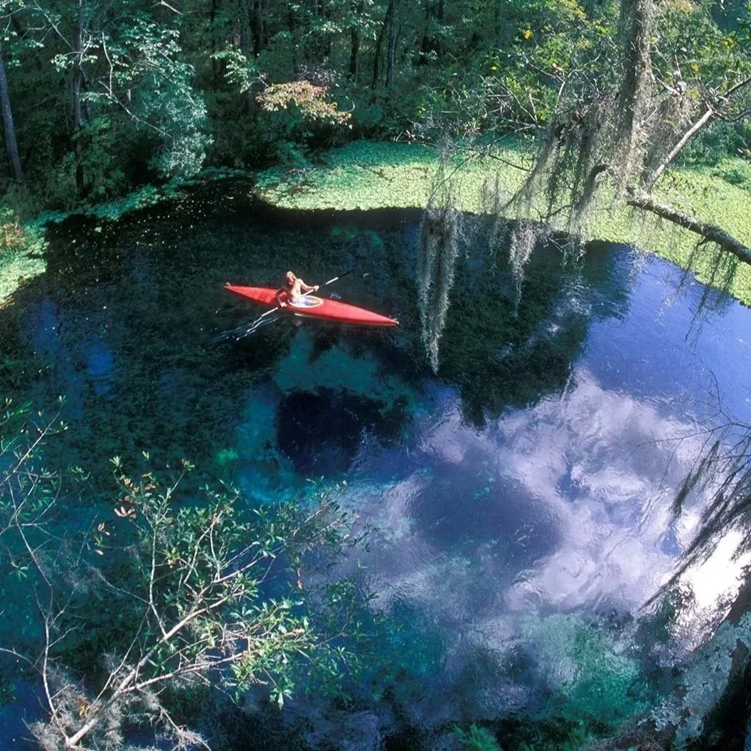 Kayaker paddling across the clear blue waters of Ichetucknee Blue Hole surrounded by forest