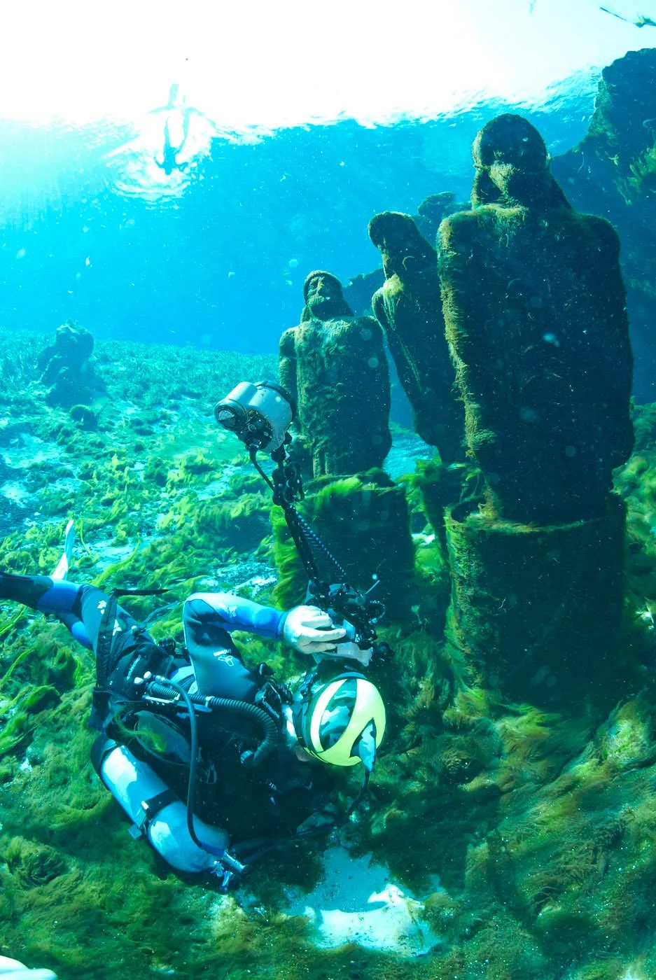 Scuba diver photographing underwater statues covered in algae in a spring