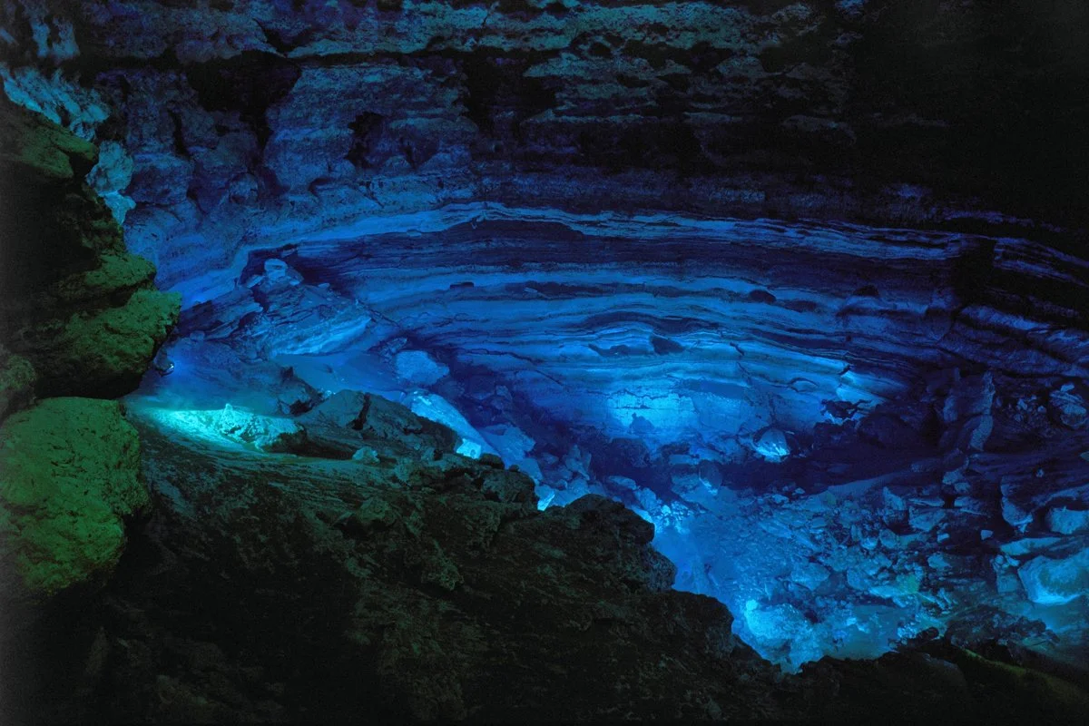 Deep, circular limestone spring basin at Silver Glen Springs illuminated in blue light, revealing layered rock walls descending into clear water.