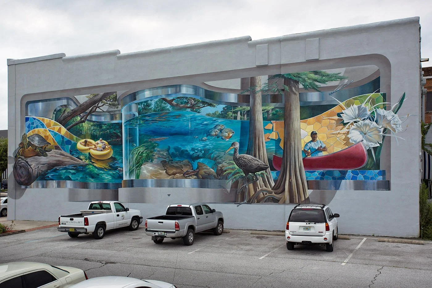 Large mural depicting the Ichetucknee River with wildlife, kayakers, and underwater scenes on a building in Lake City, Florida