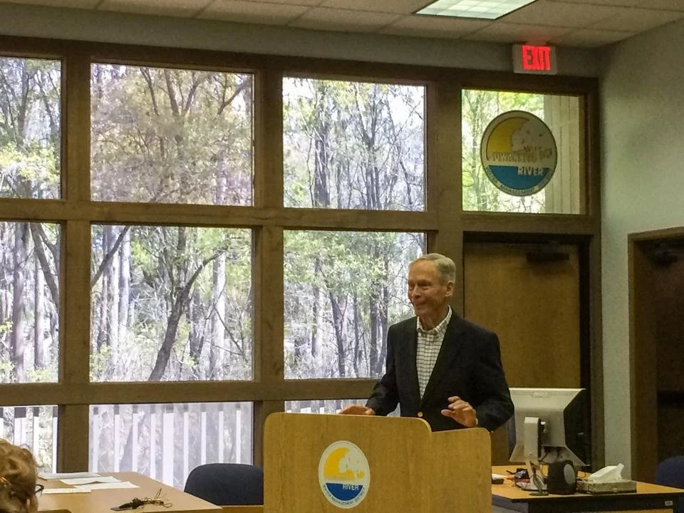 Former Florida Governor Buddy MacKay Jr. speaking at a public meeting in a conference room.