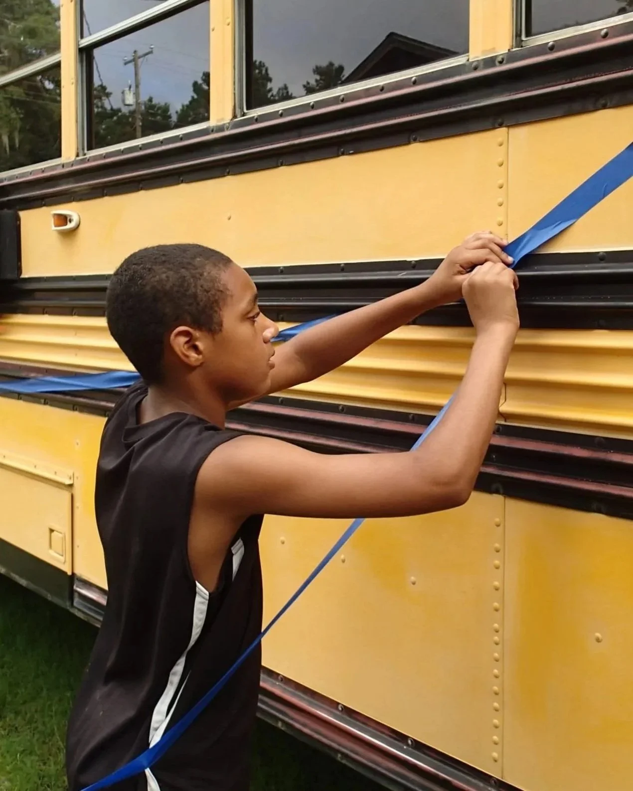 Student applying painter’s tape to a bus surface in preparation for a mural design.