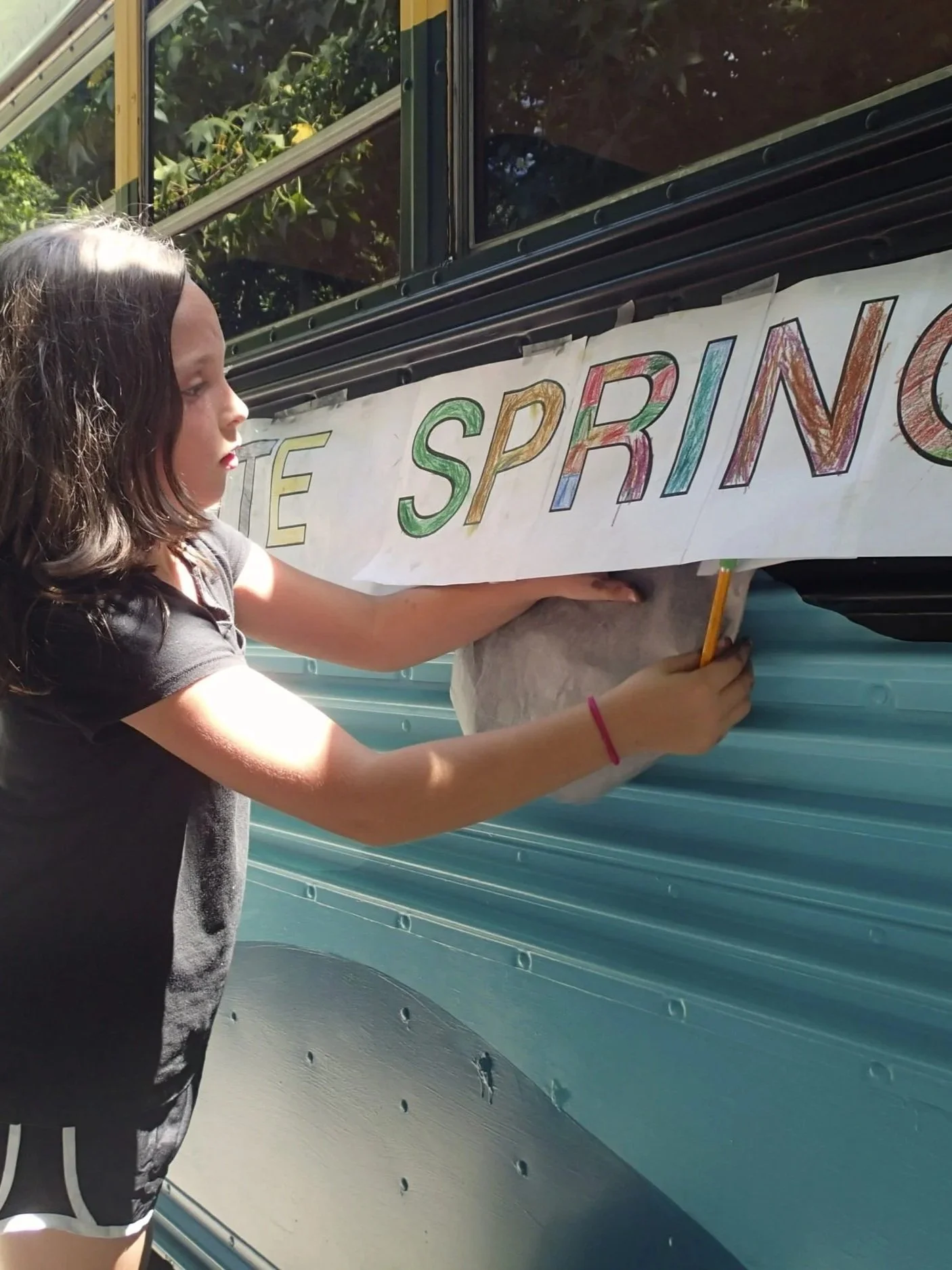 Child aligning and attaching lettering to a bus exterior as part of a collaborative springs-themed mural.