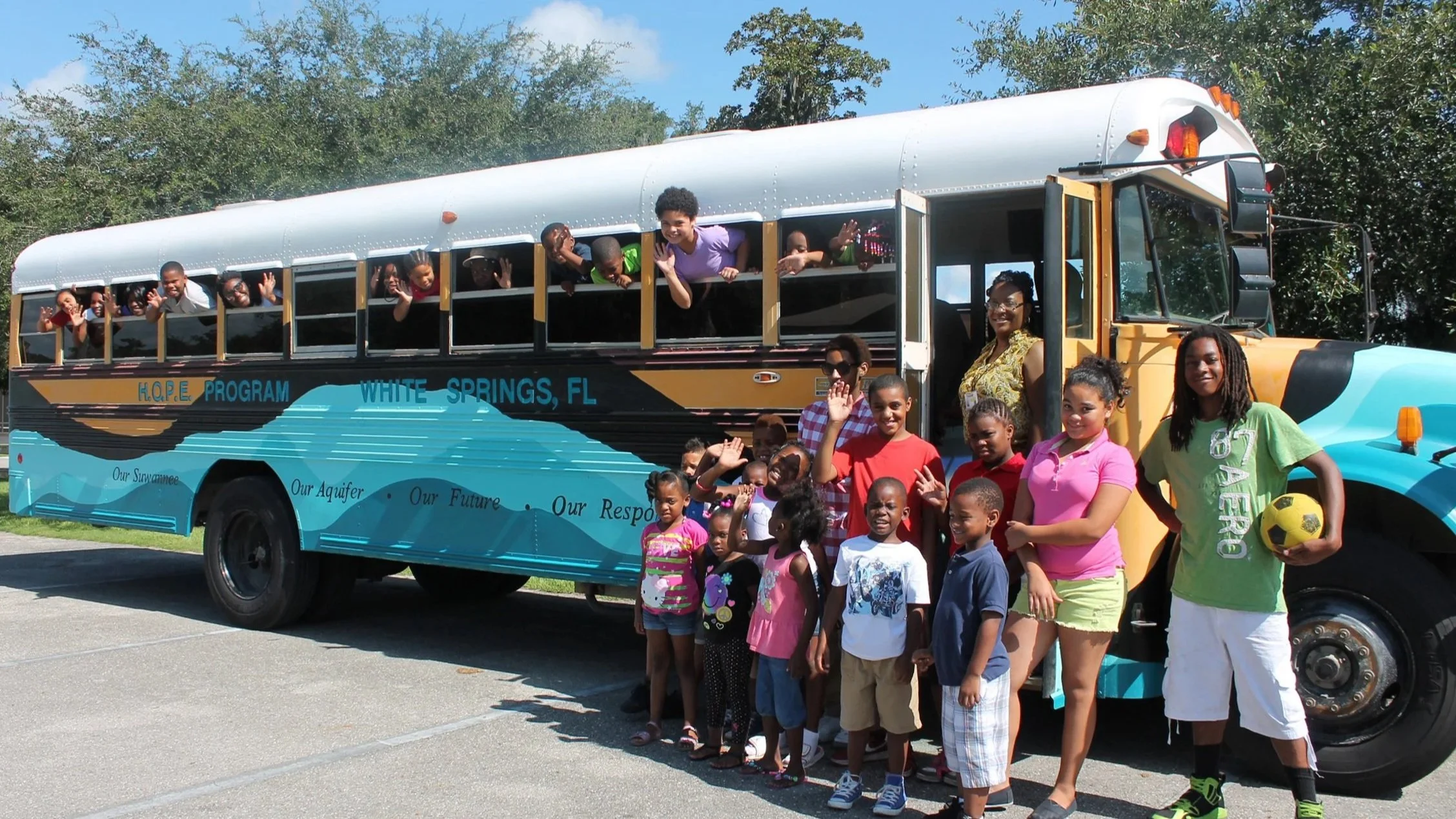 Students standing in front of and hanging out of the windows of a painted Rural Aquifer bus