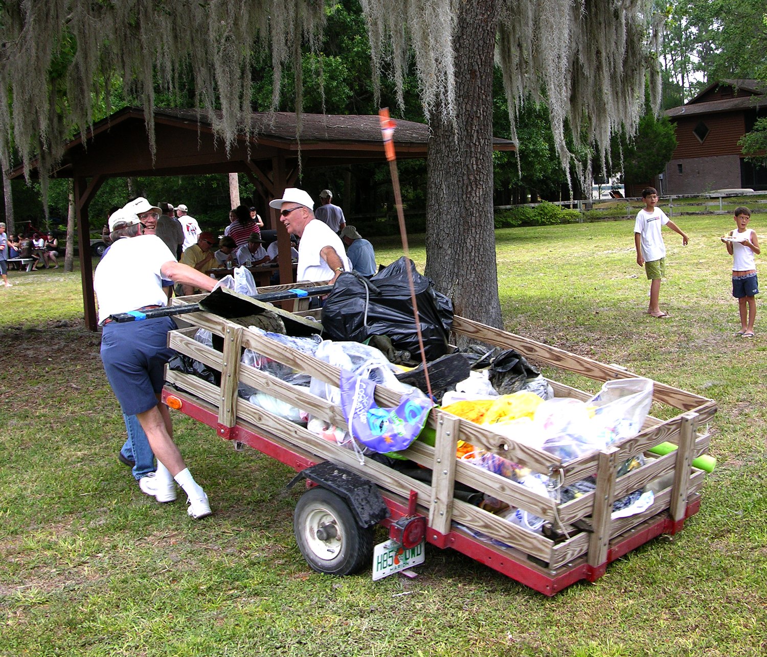 Volunteers loading collected trash bags onto a small trailer during a river cleanup event in a park