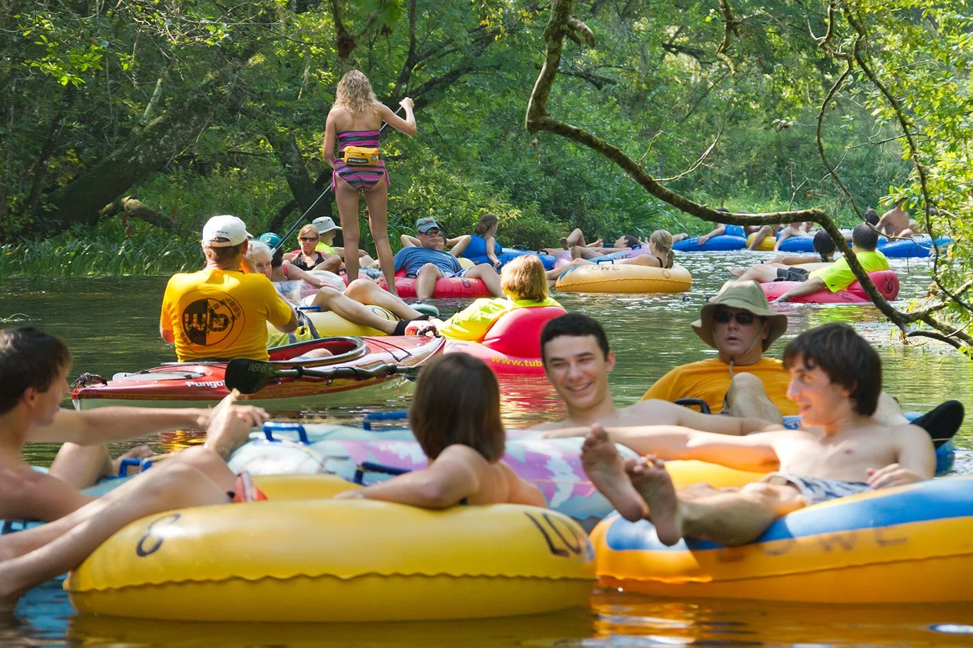 Group of people floating on inner tubes along a tree-lined spring run, relaxing and socializing on the water