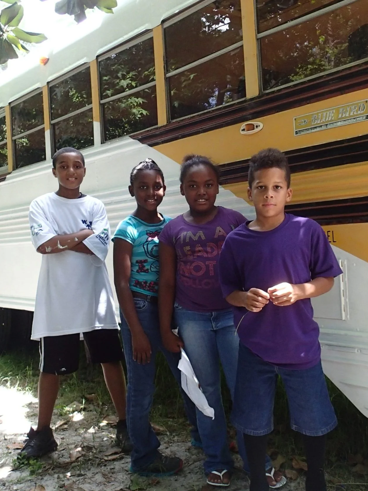 Group of children standing in front of a bus, participating in a community-based art and environmental project.