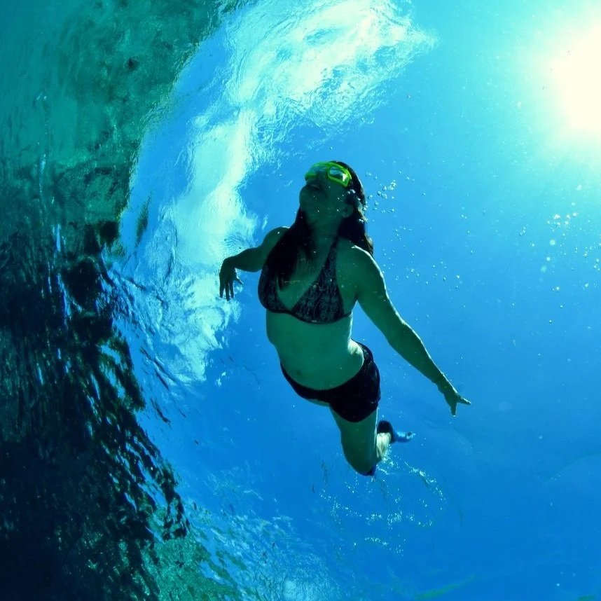 Woman snorkeling underwater in clear blue spring water with sunlight above