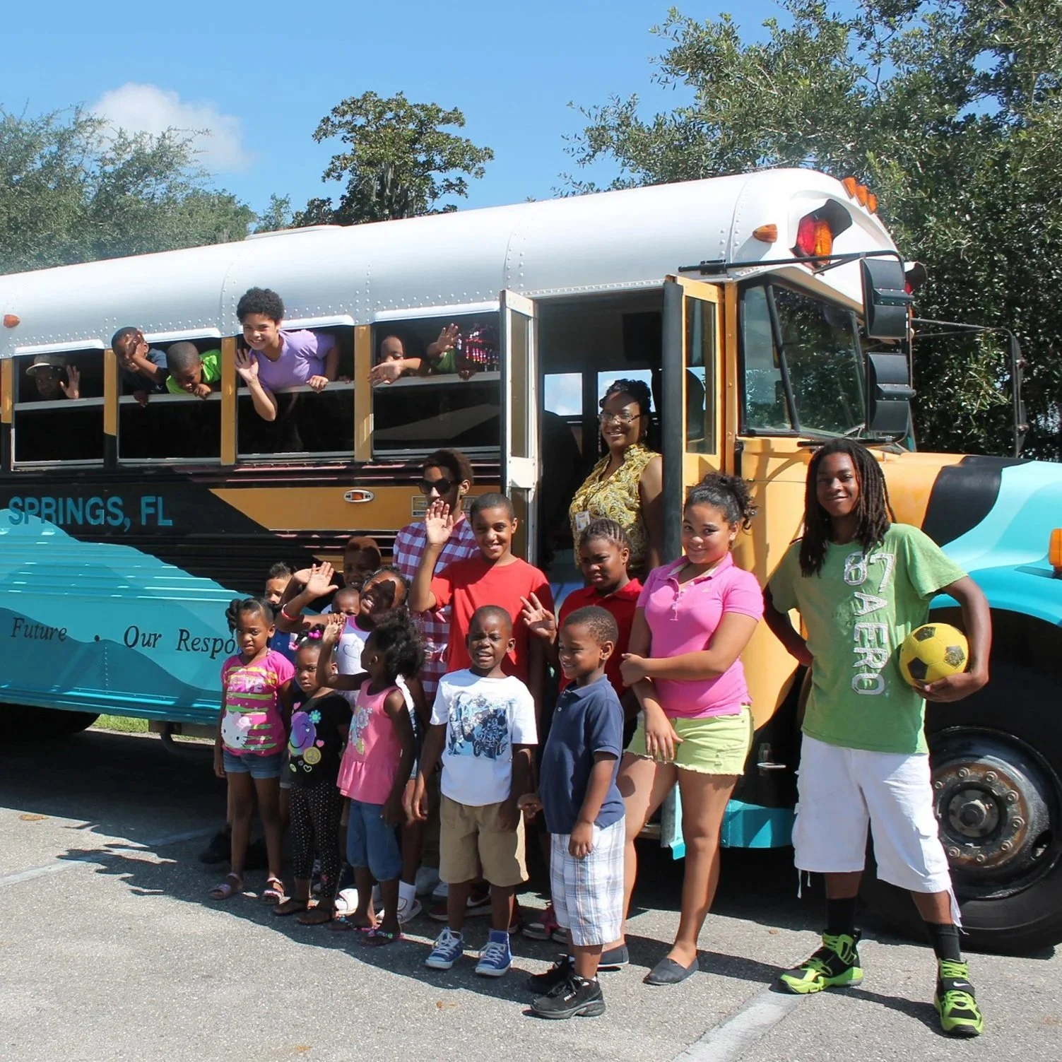 Group of children and adults waving beside a bus from the H.O.P.E. Program in White Springs, Florida, promoting awareness of the Suwannee River and Floridan aquifer.