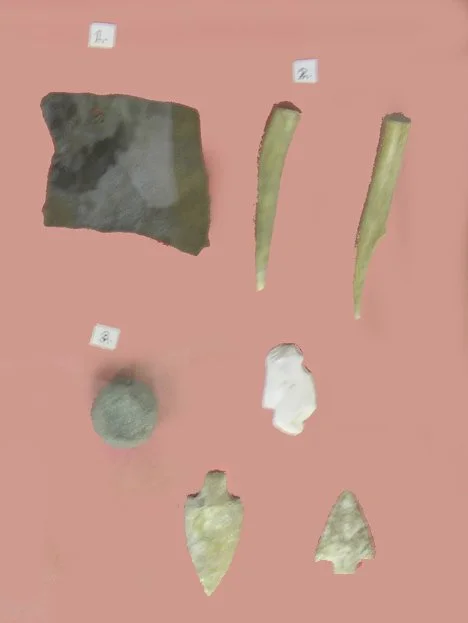 Assorted prehistoric stone tools and artifacts, including arrowheads and fragments, displayed against a plain background, representing items found in the Rainbow Springs area.