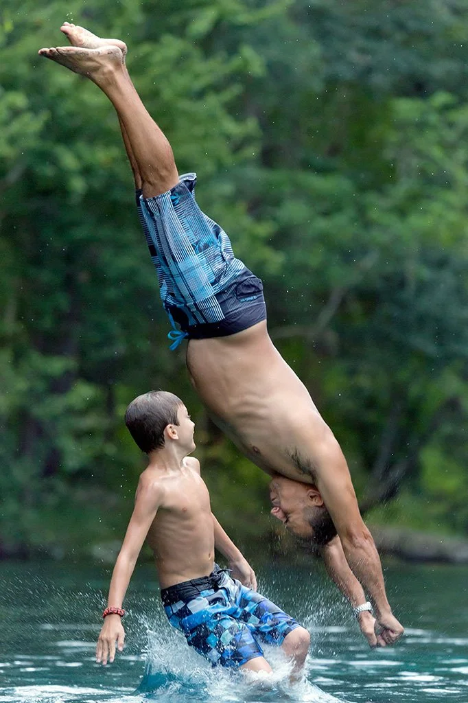 Two campers jumping and diving in to the spring.
