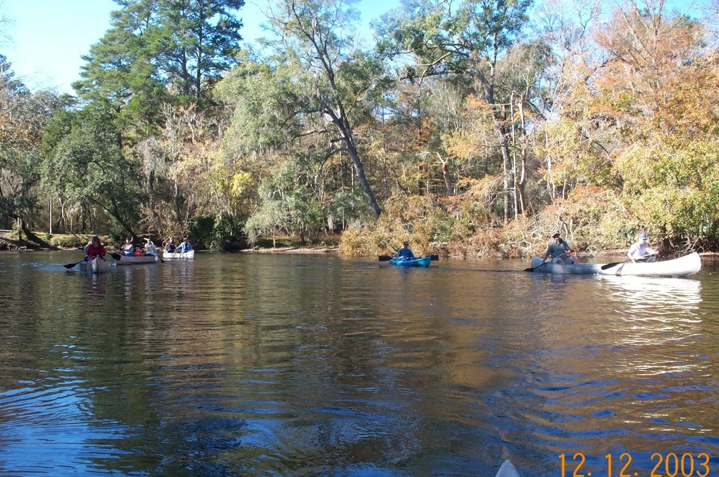 People kayaking along a tree-lined river connected to the spring