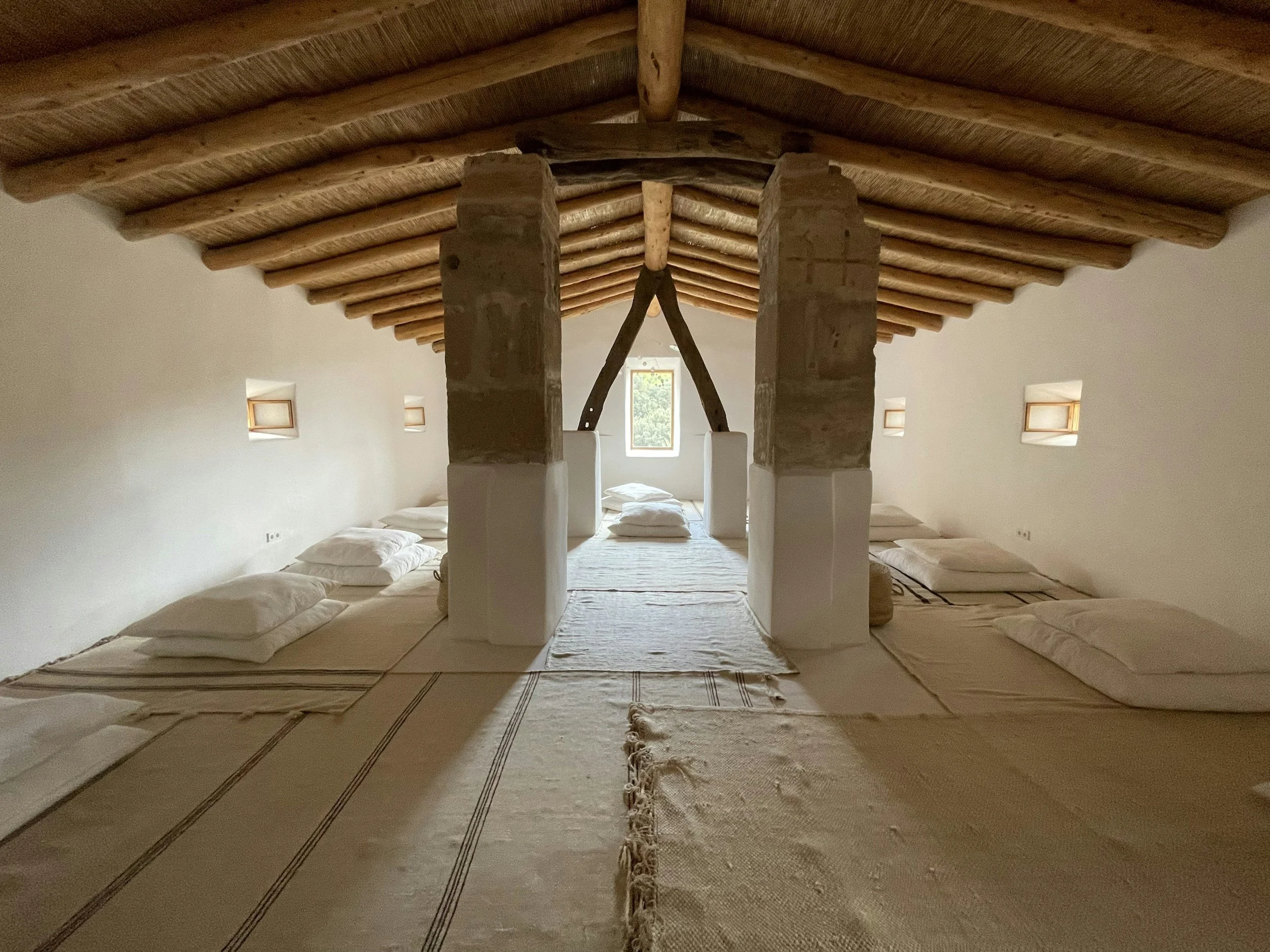 Tomorrow House retreats. Photo of tranquil retreat space with high wooden beamed ceiling and white meditation cushions against muted natural light.
