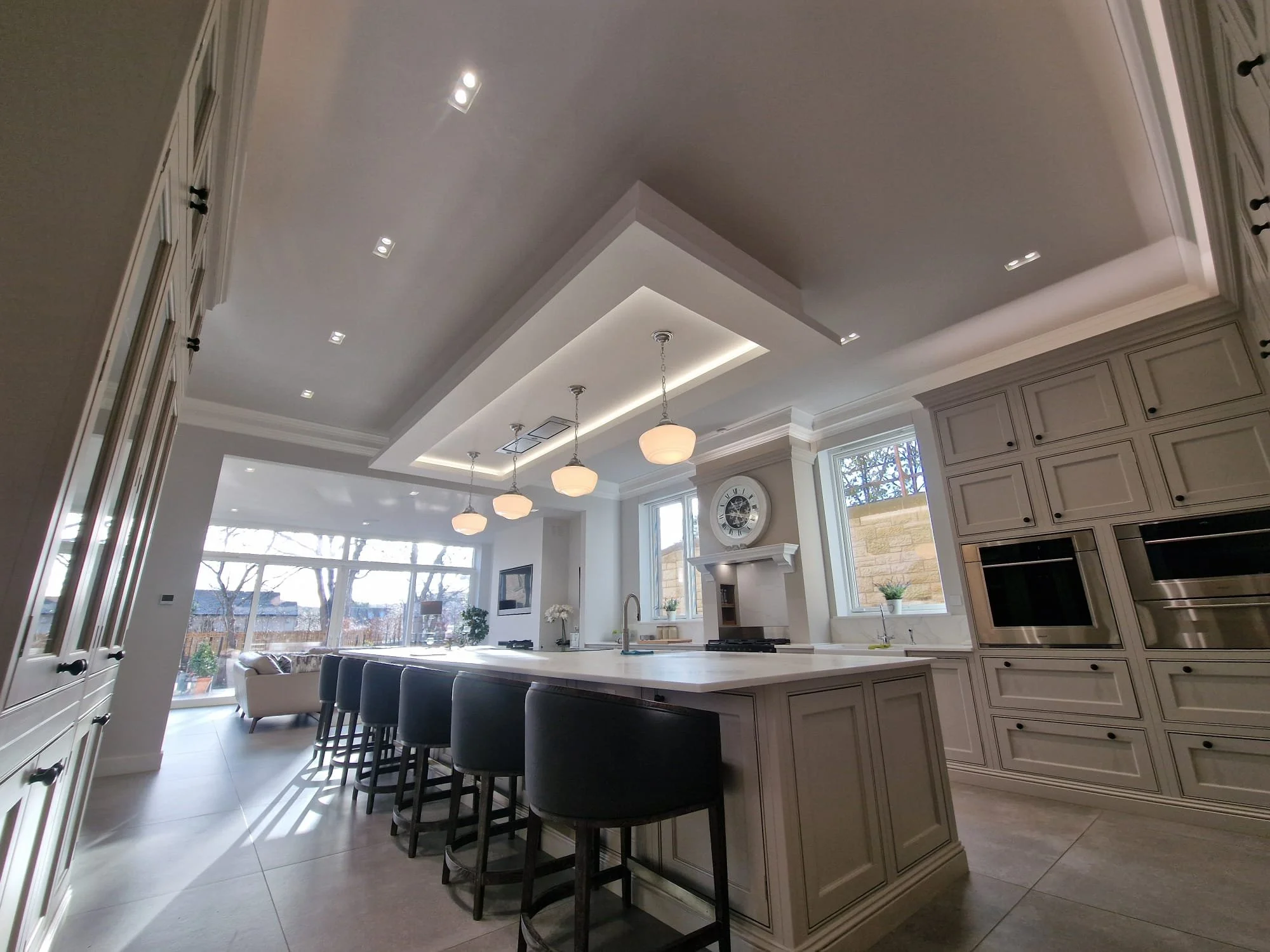 Bright modern kitchen with white cabinetry, large island with black barstools, built-in microwave, and large windows letting in natural light.