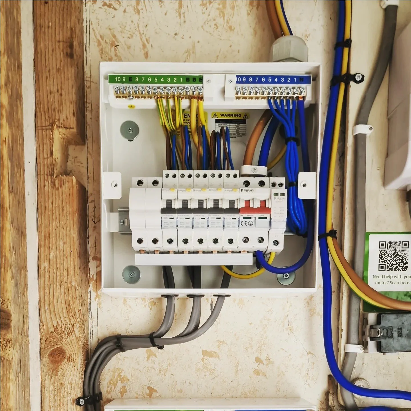 Electrical switchboard with wiring, circuit breakers, and colored wires installed inside a white box on a wall.