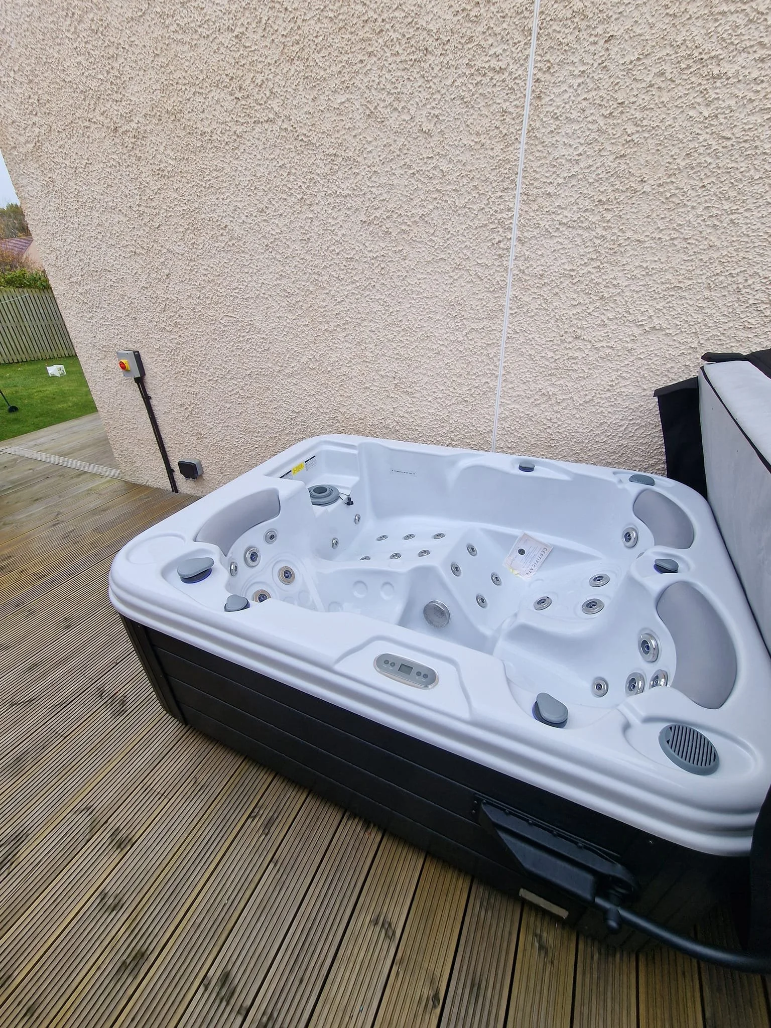 White hot tub on a wooden deck outside next to a beige stucco wall.