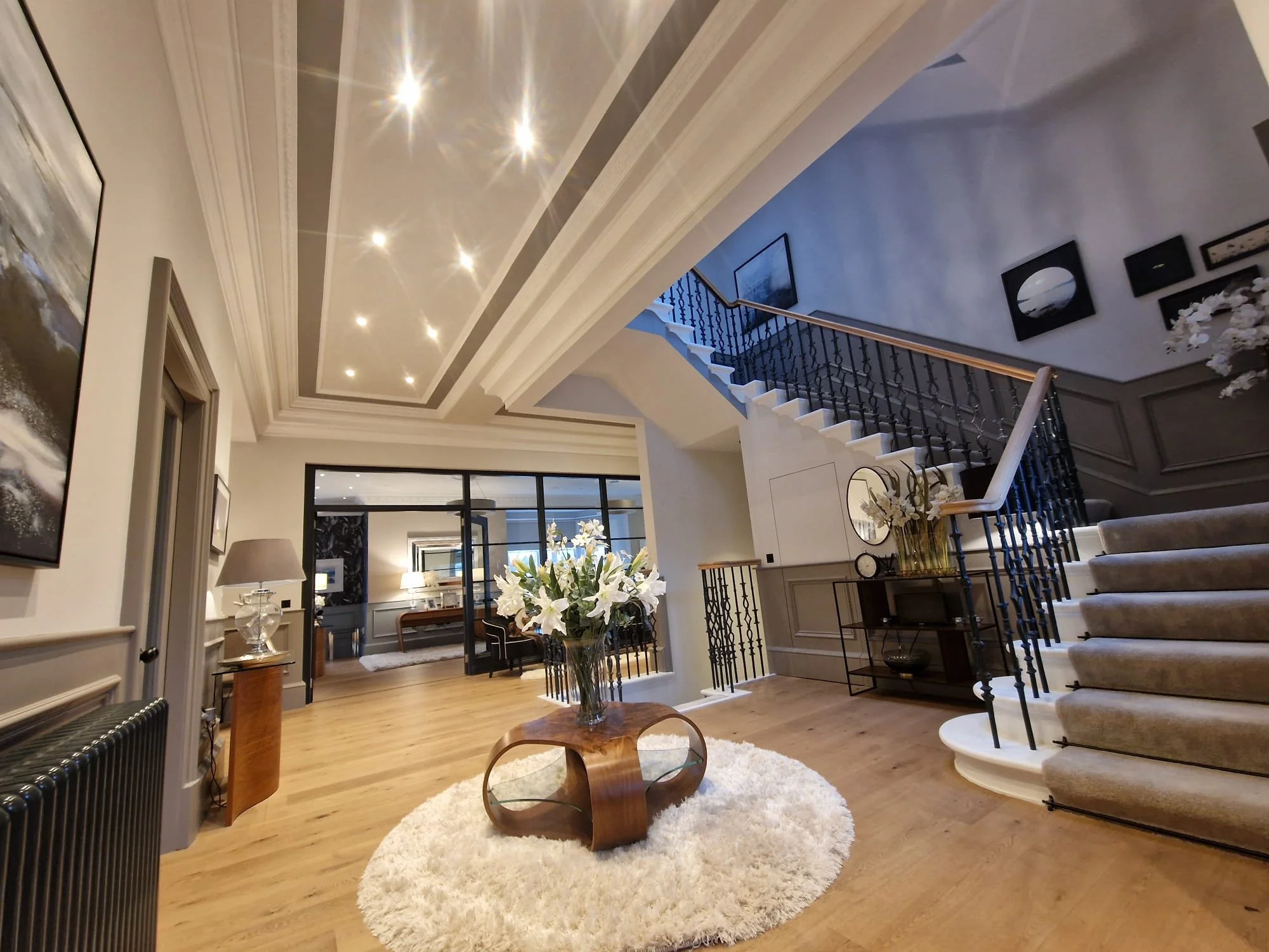 Elegant entryway with a curved staircase, light hardwood floors, floral arrangements, and modern art on the walls.