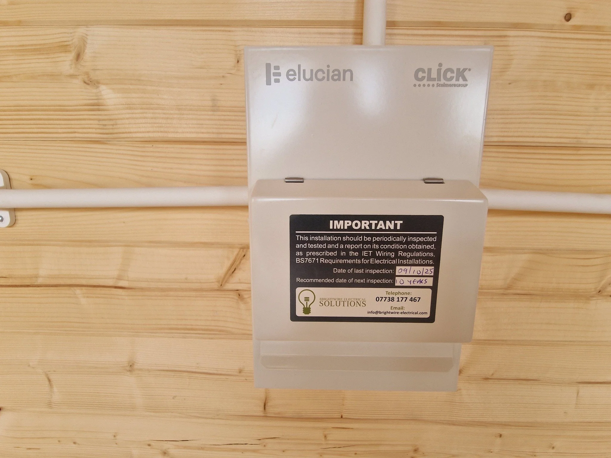 Electrical panel mounted on wooden wall with white conduit pipe running horizontally.