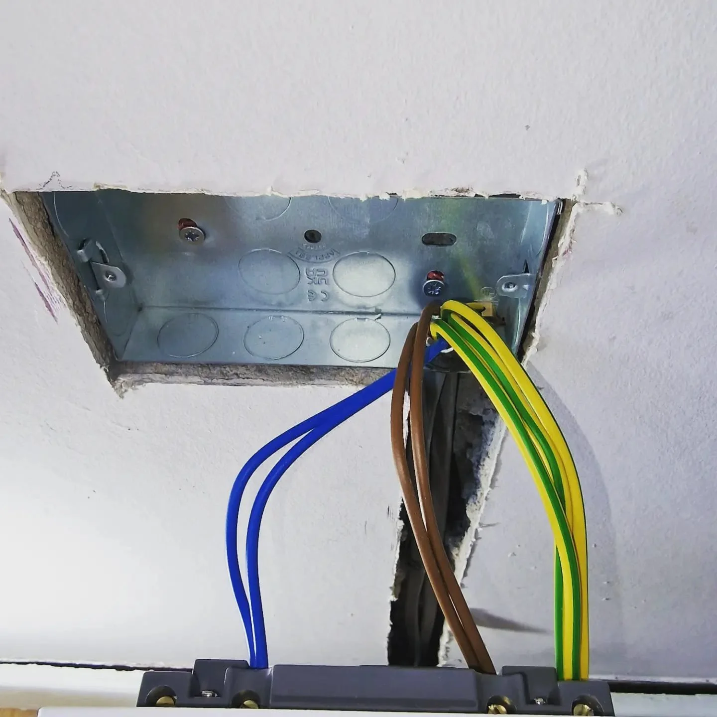 Electrical wiring in a ceiling junction box with blue, brown, and yellow-green striped wires.