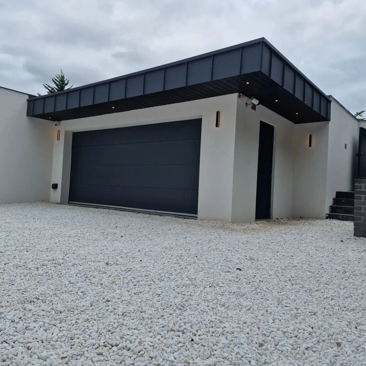 Modern house with a black garage door, white exterior walls, black accents, and stone steps, surrounded by white gravel.