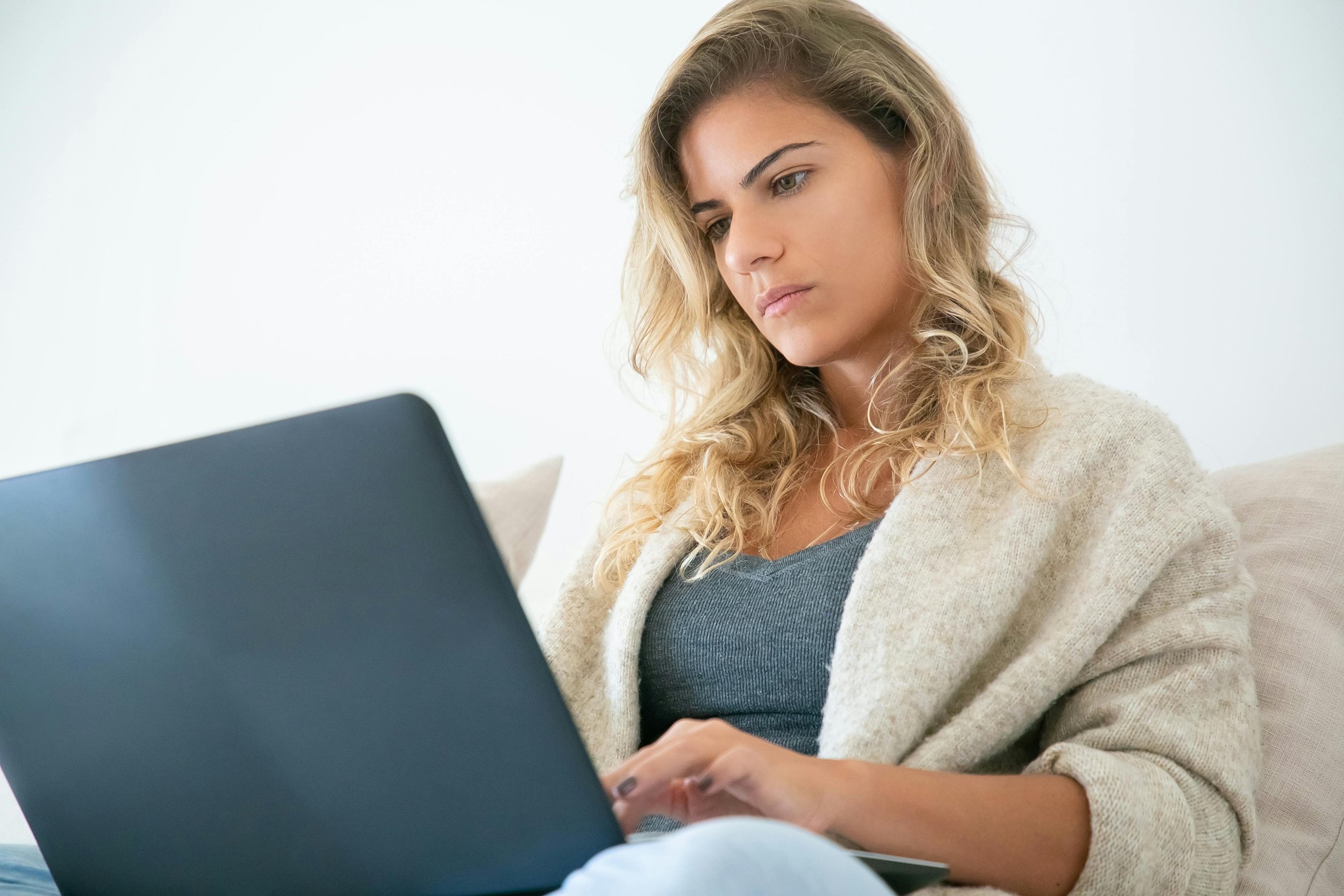 A woman with blonde hair sitting on a couch using a laptop.
