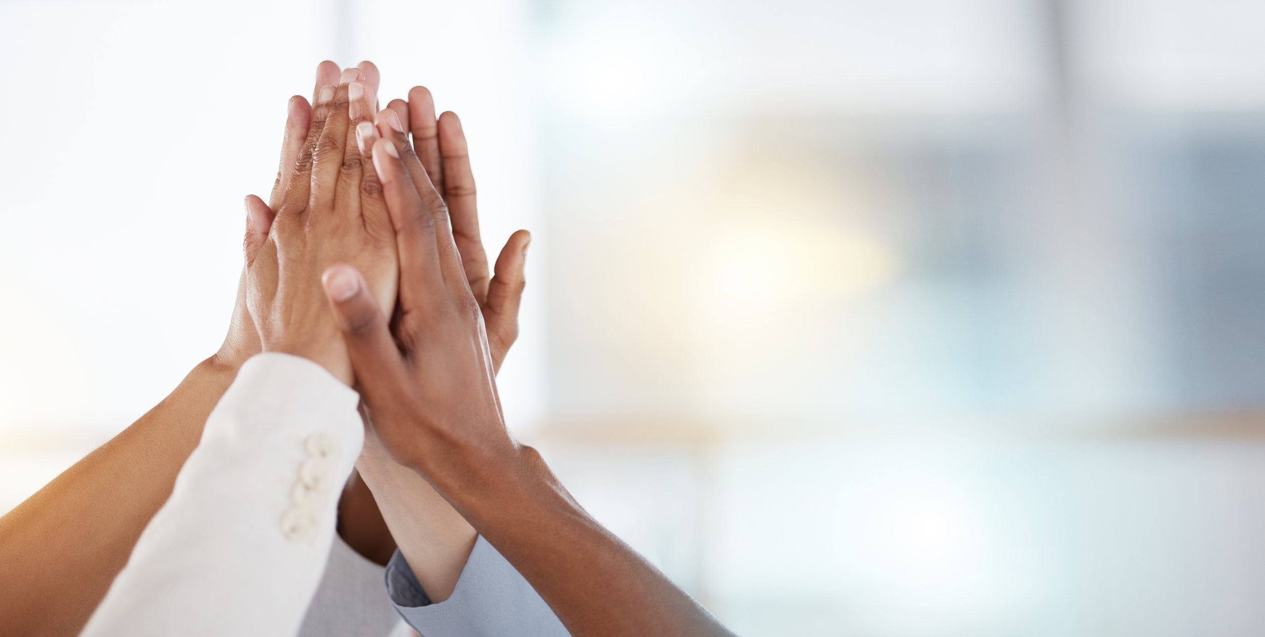 Two people in professional attire with clasped hands in a gesture of unity or greeting, blurred background.