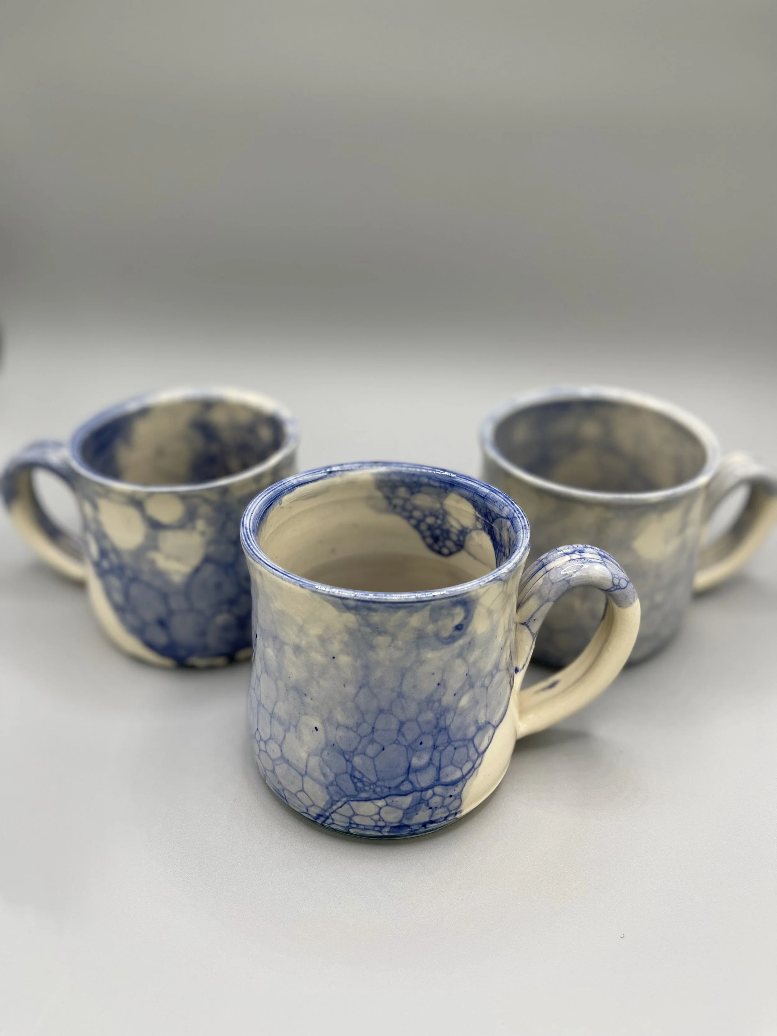 Three ceramic mugs with blue and cream marbled glaze on a light surface.