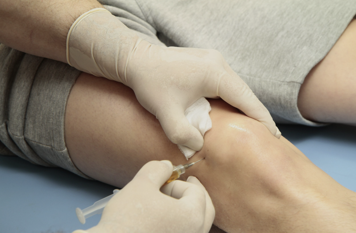 A medical professional is administering a shot into a patient's arm, with a cotton ball and gloved hands visible.