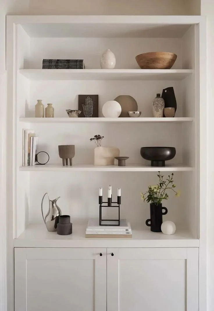 White shelving unit with decorative objects including vases, bowls, books, and a candle holder.