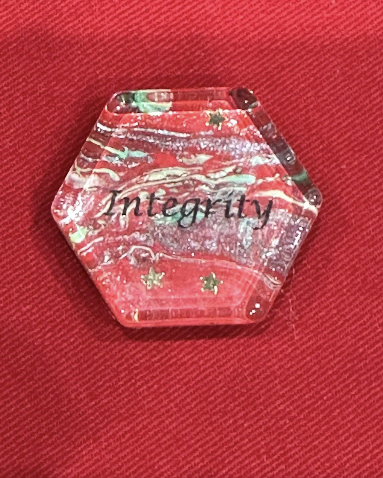 closeup of hand painted motivational magnet with the word integrity shaped in a hexagon with gold stars