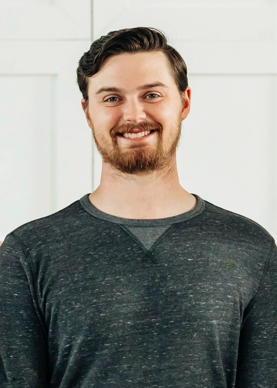 Justin Kuglin, owner of Prismadic Studios, wearing a dark gray sweatshirt, standing in front of a plain, light-colored background.
