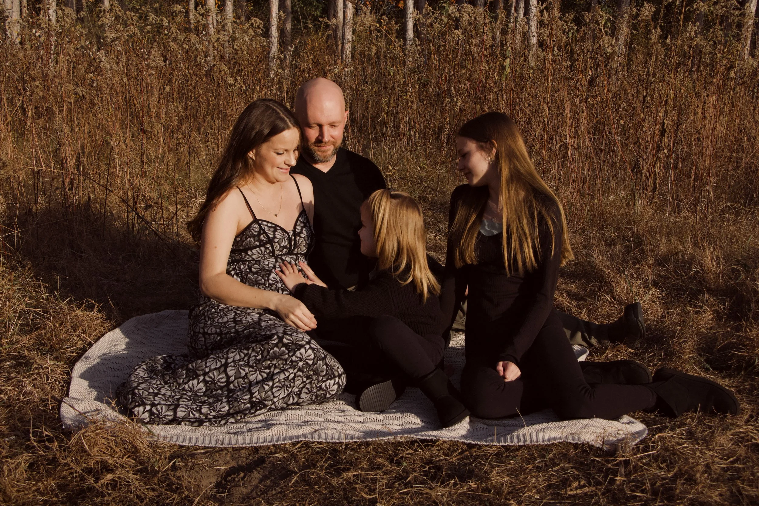 Family of four sitting together on a blanket in a sunlit autumn meadow