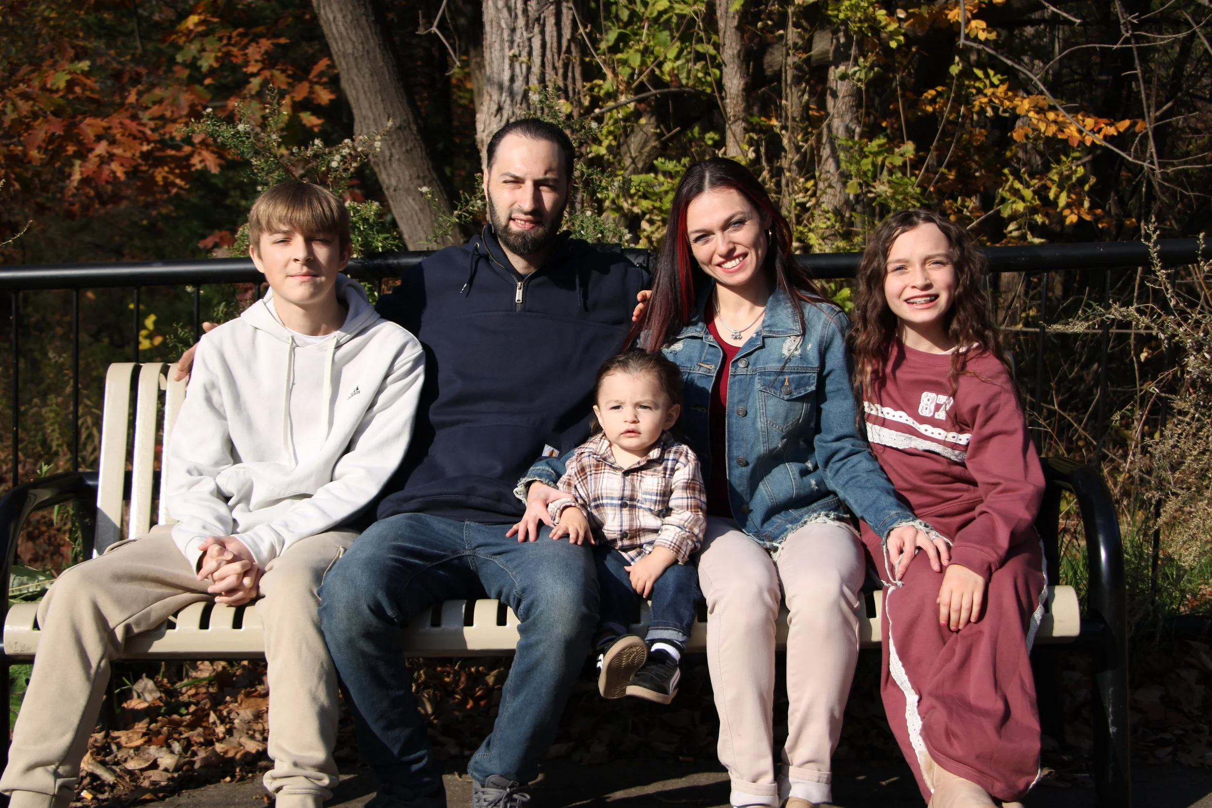 Family of five sitting on a park bench surrounded by autumn trees