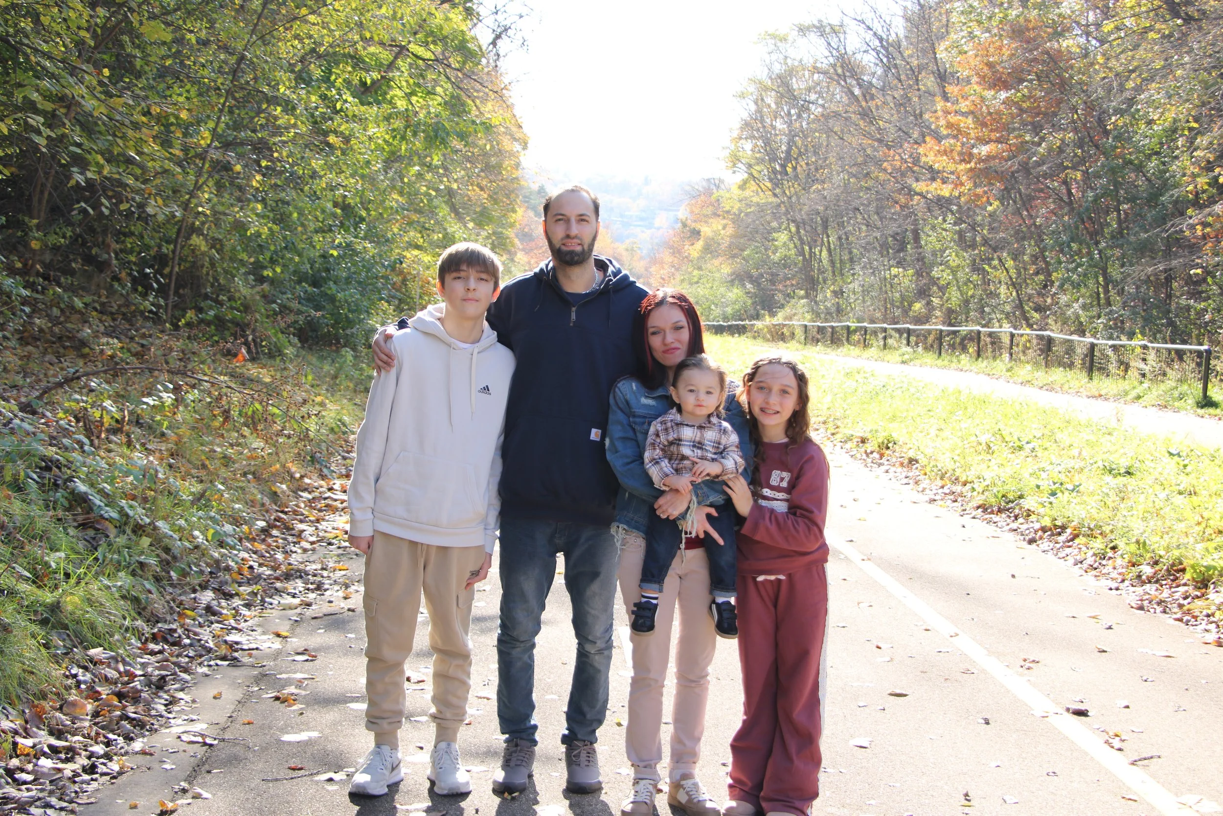 Family of five posing on a paved trail surrounded by colorful autumn trees