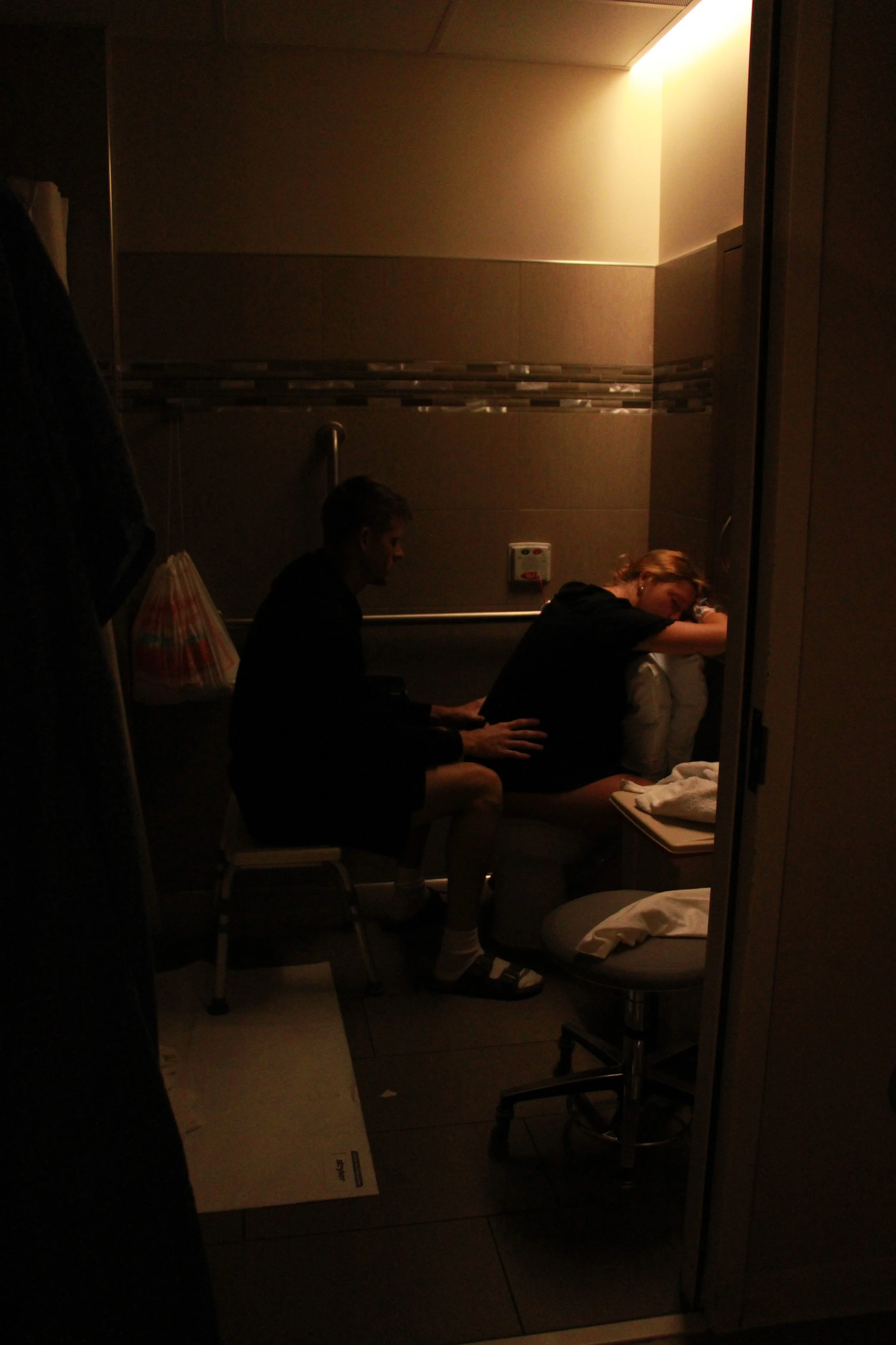 People seated inside a dimly lit elevator with tiled walls, handrails, and a fold-down seat.